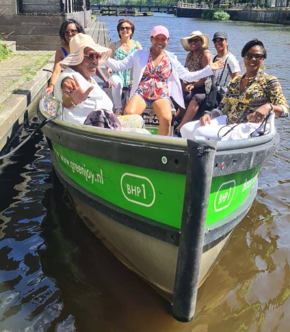 Six women sitting in a small boat on the water, smiling and enjoying a boat ride.