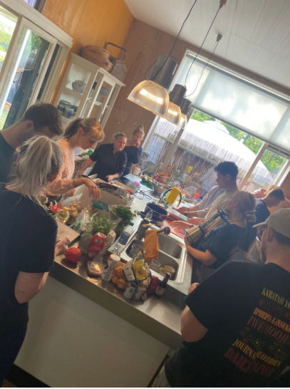 Group of people gathered in a kitchen, preparing and cooking food together around a kitchen island.