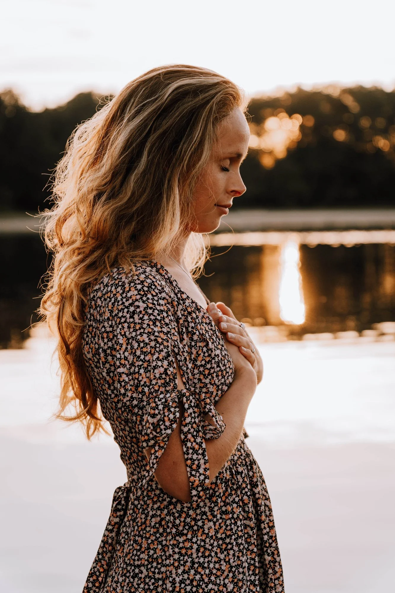 Aanbevolen alt text:  Vrouw in verstilling met handen op haar hart bij zonsondergang aan het water.  Iets SEO-gerichter voor de retreatpagina:  Marinda van Praktijk Natuurwezen in verstilling bij het water voor het Sovereign Soul Activation Retreat b