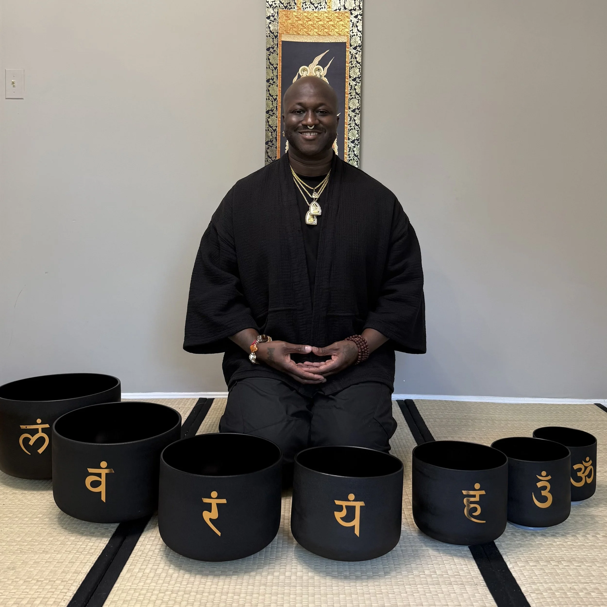 Born I zit in kleermakerszit op een tatami-mat in een zwart kimonovest, met voor hem een halve cirkel van zeven zwarte klankschalen met gouden chakrasymbolen.