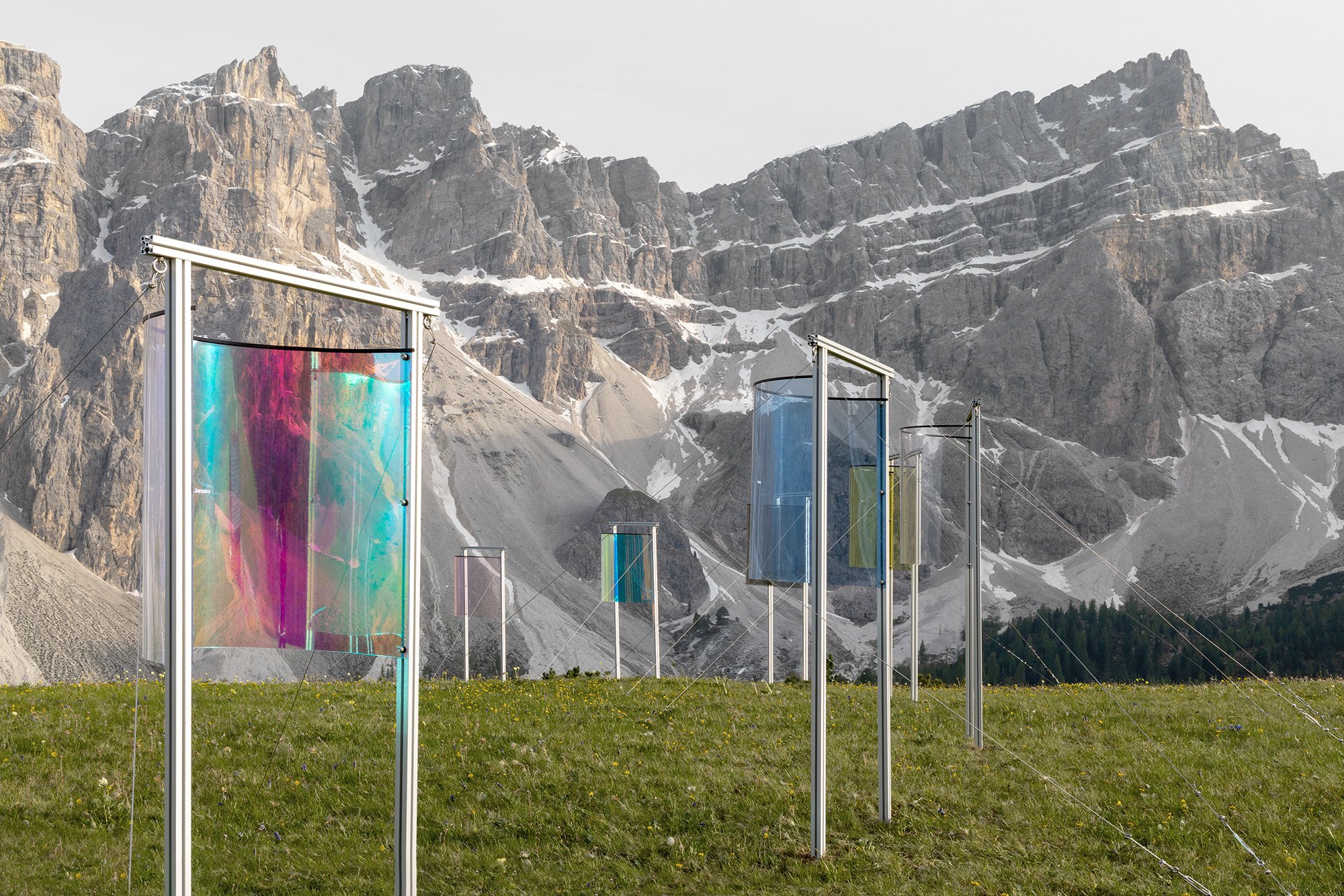 Colorful fabric wind art installation on a grassy field with mountain cliffs in the background.