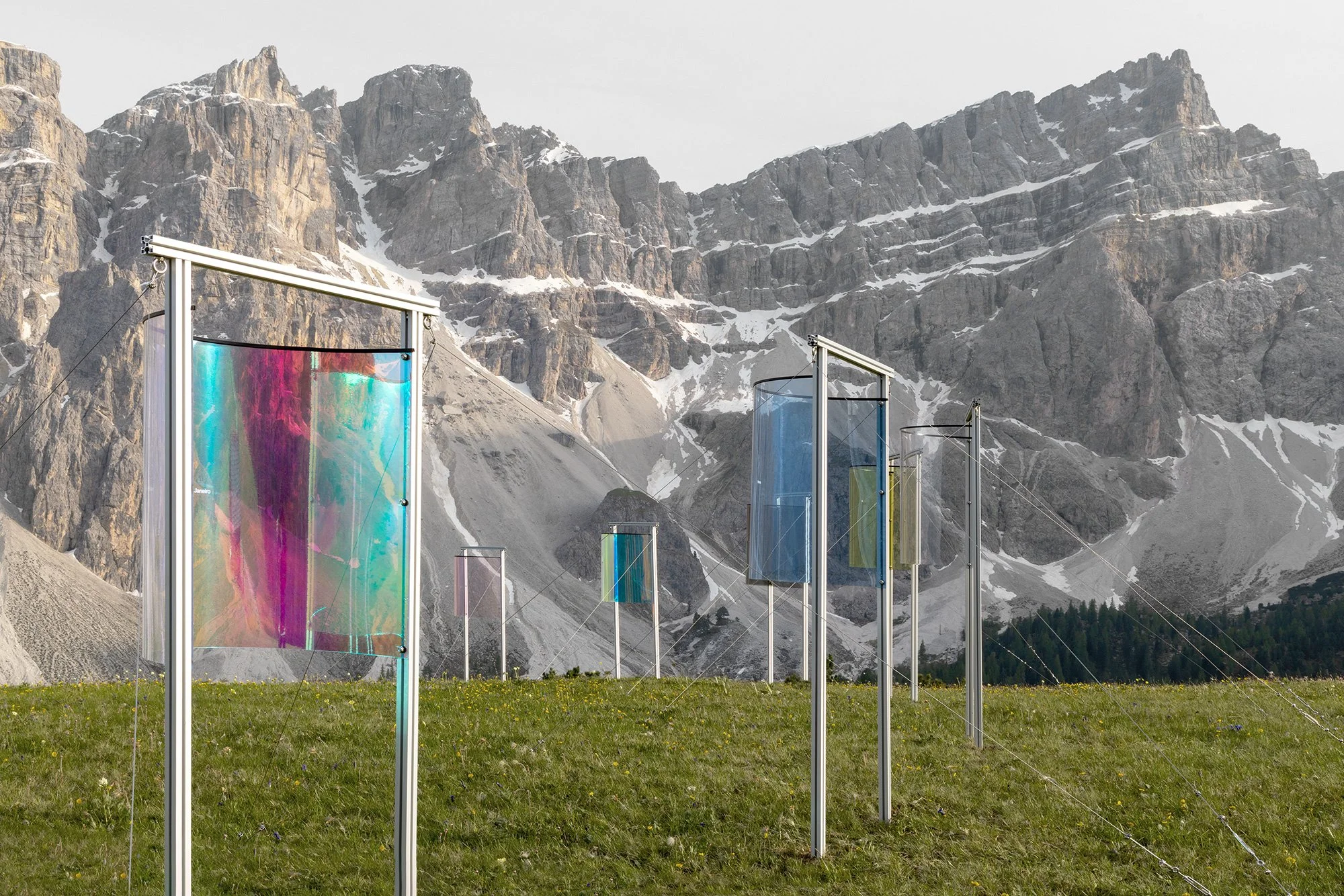 An installation of tall frames with colorful panels stands in a field with mountains behind.