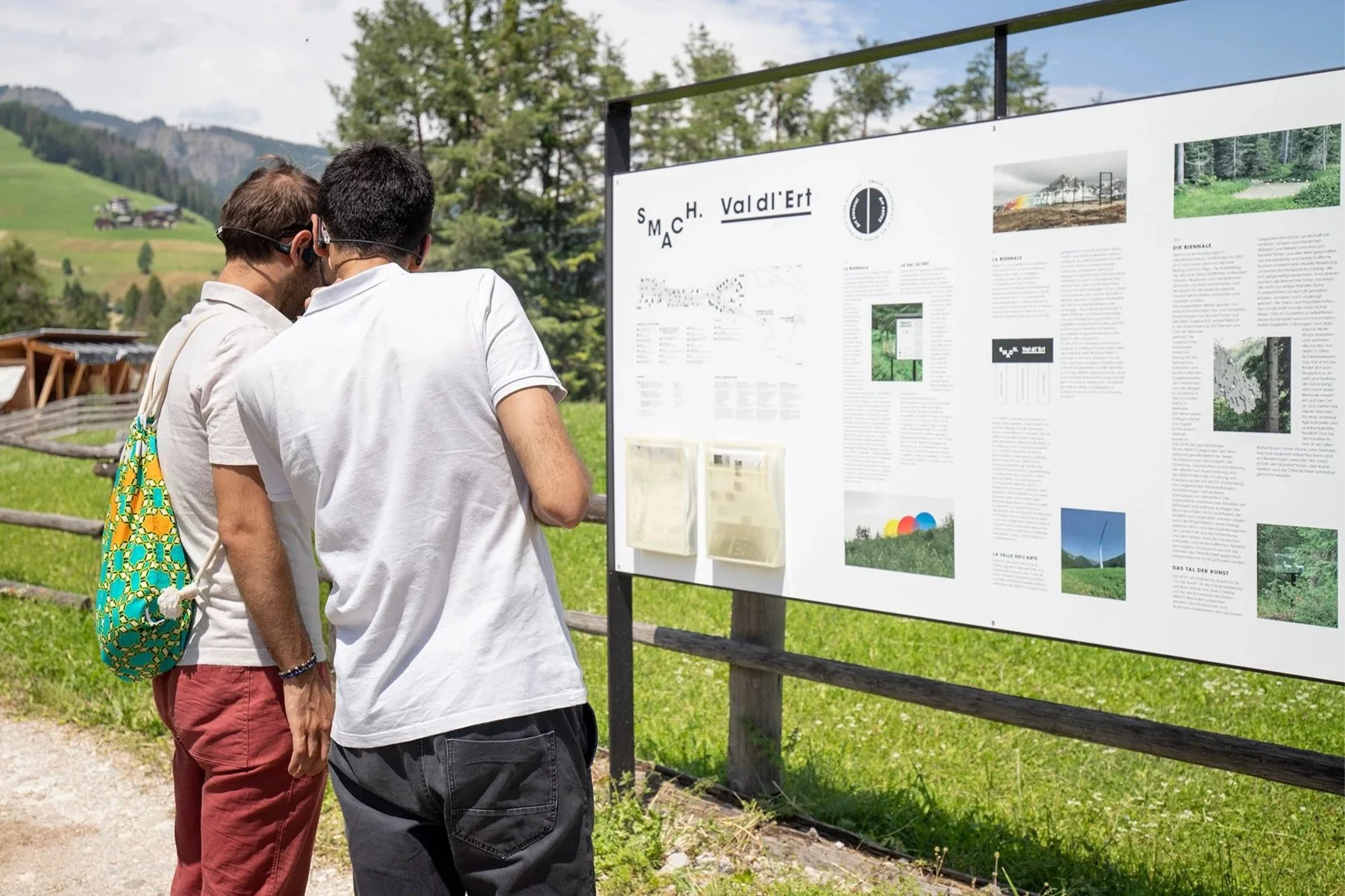 Two visitors examine a "SMACH. Val d'Ert" information board featuring maps and project details.