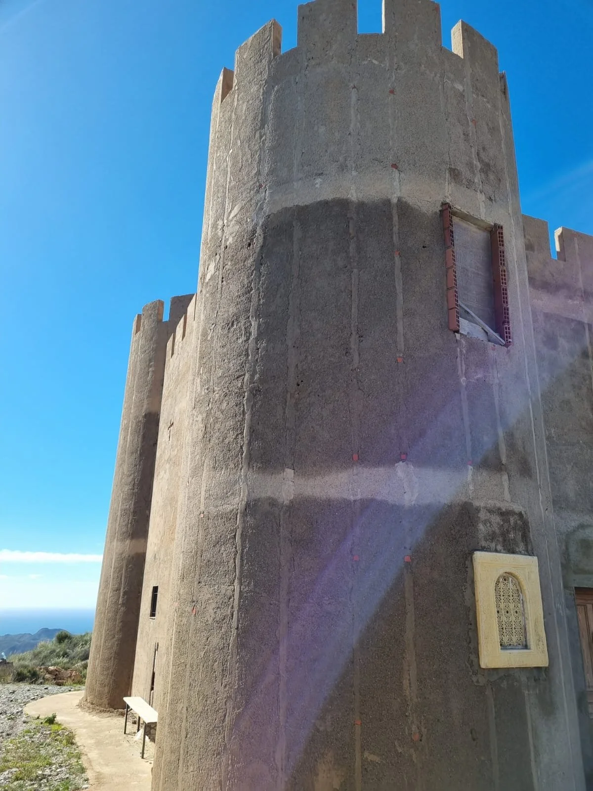 Burgmauer aus rotem Stein in der Sonne mit blauer Himmel im Hintergrund.