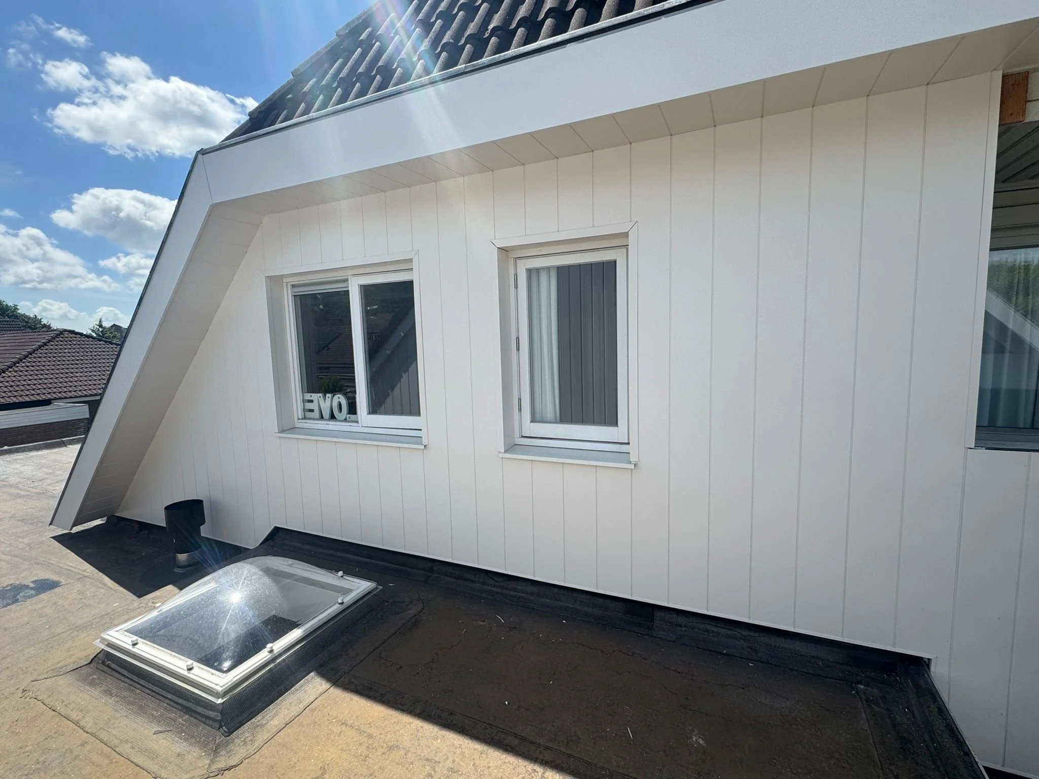 White exterior wall of a building with two windows, a skylight on the roof, and a cloudy blue sky.