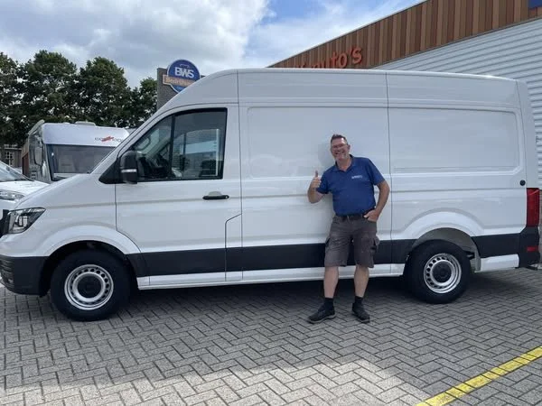A smiling man standing beside a white cargo van giving a thumbs-up in a parking lot.