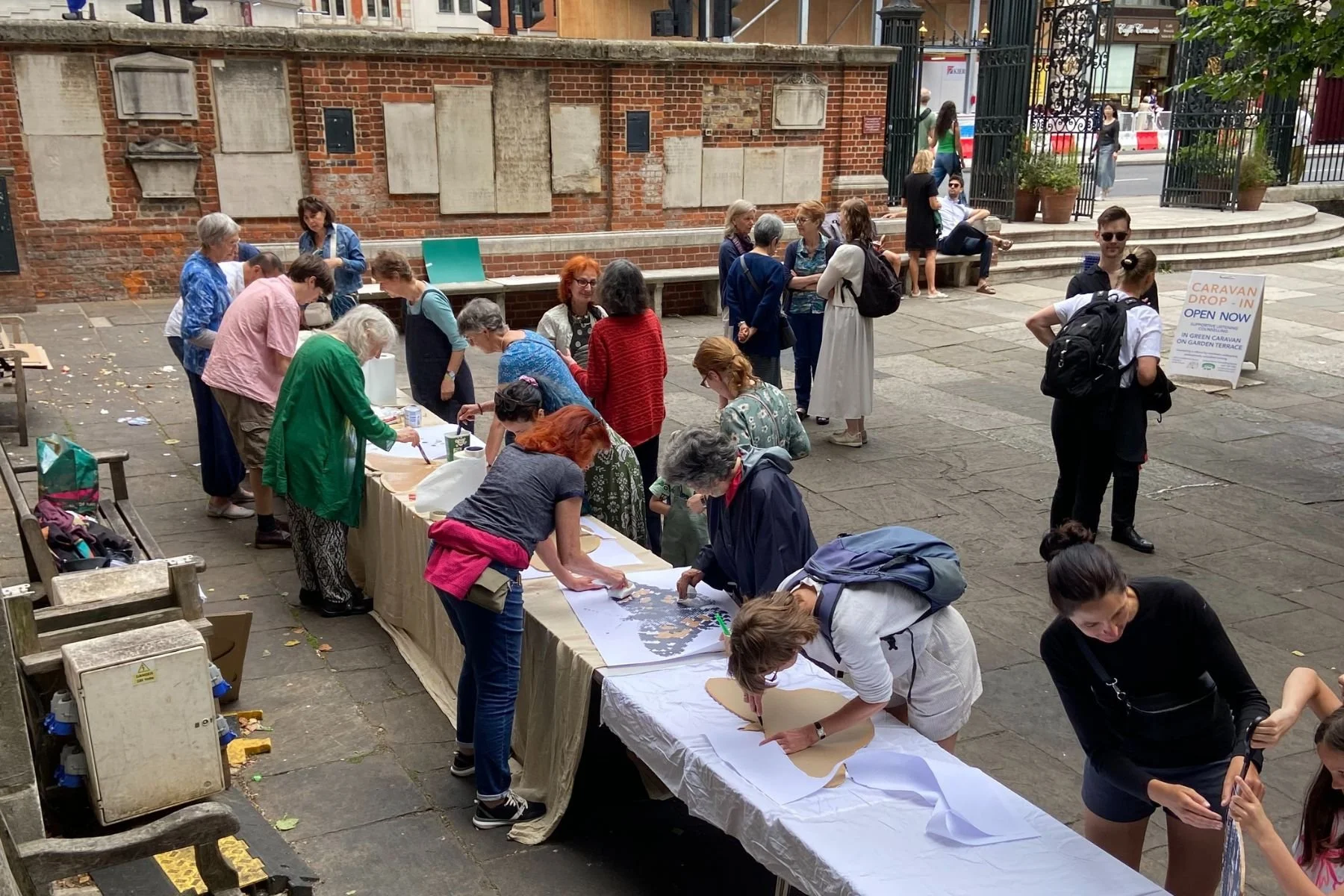 A overhead shot of St James Piccadilly's outdoor courtyard. There are a long trestle table and people are making and painting cardboard butterfly shapes as part of the SWARM project.