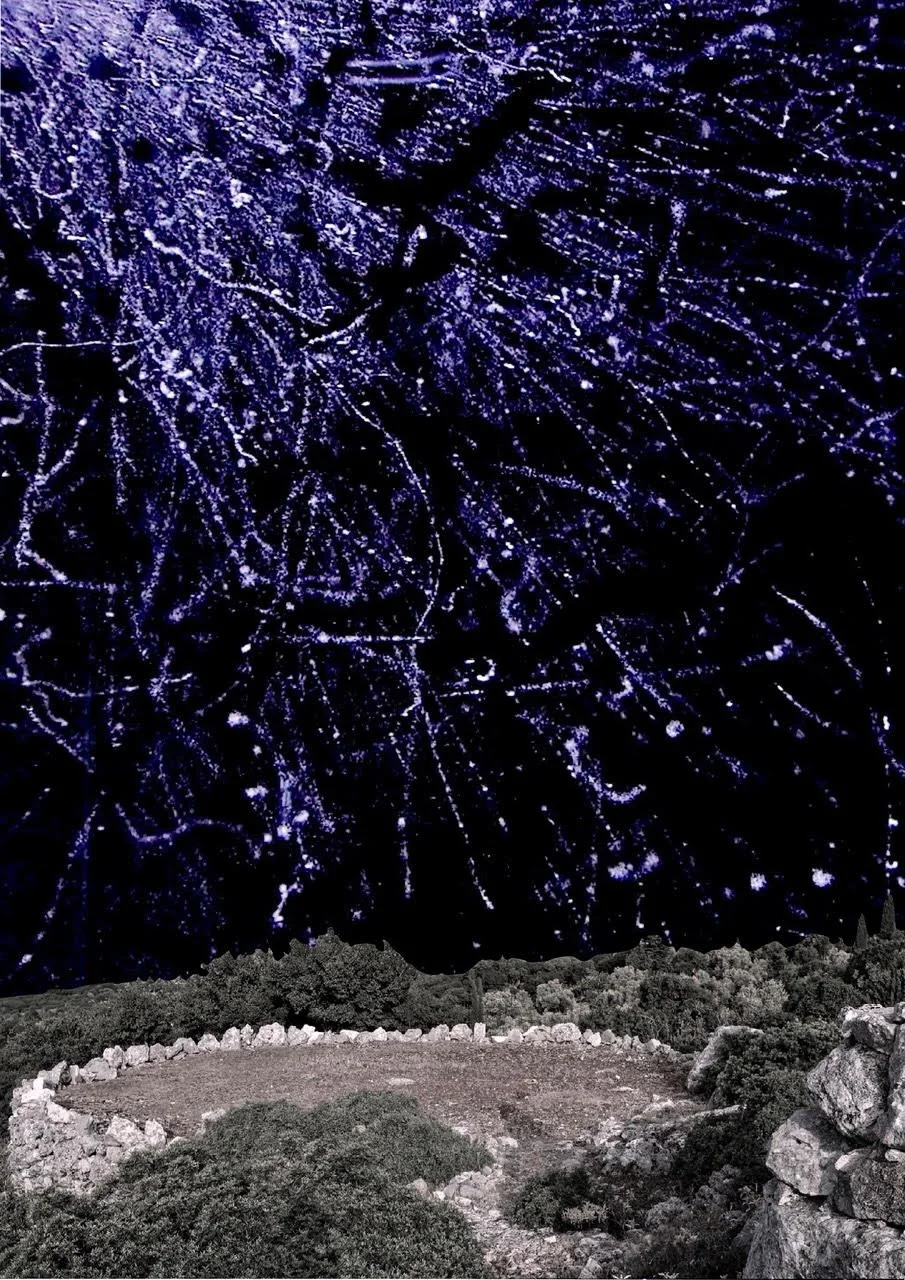 Nighttime scene with a cleared circular area surrounded by rocks and bushes, overlooking a dark landscape under a sky illuminated with colorful fireworks.