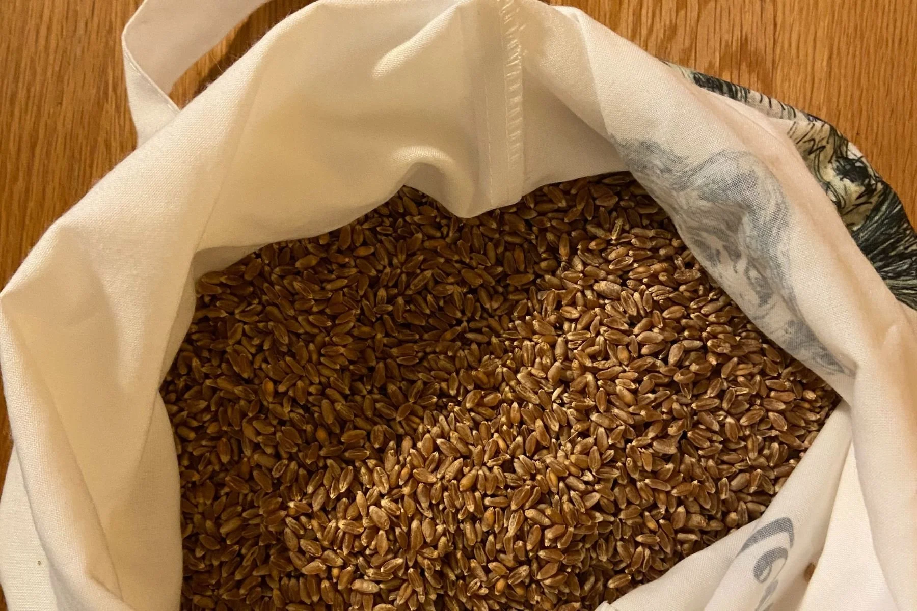 Open cloth bag filled with brown wheat grains.
