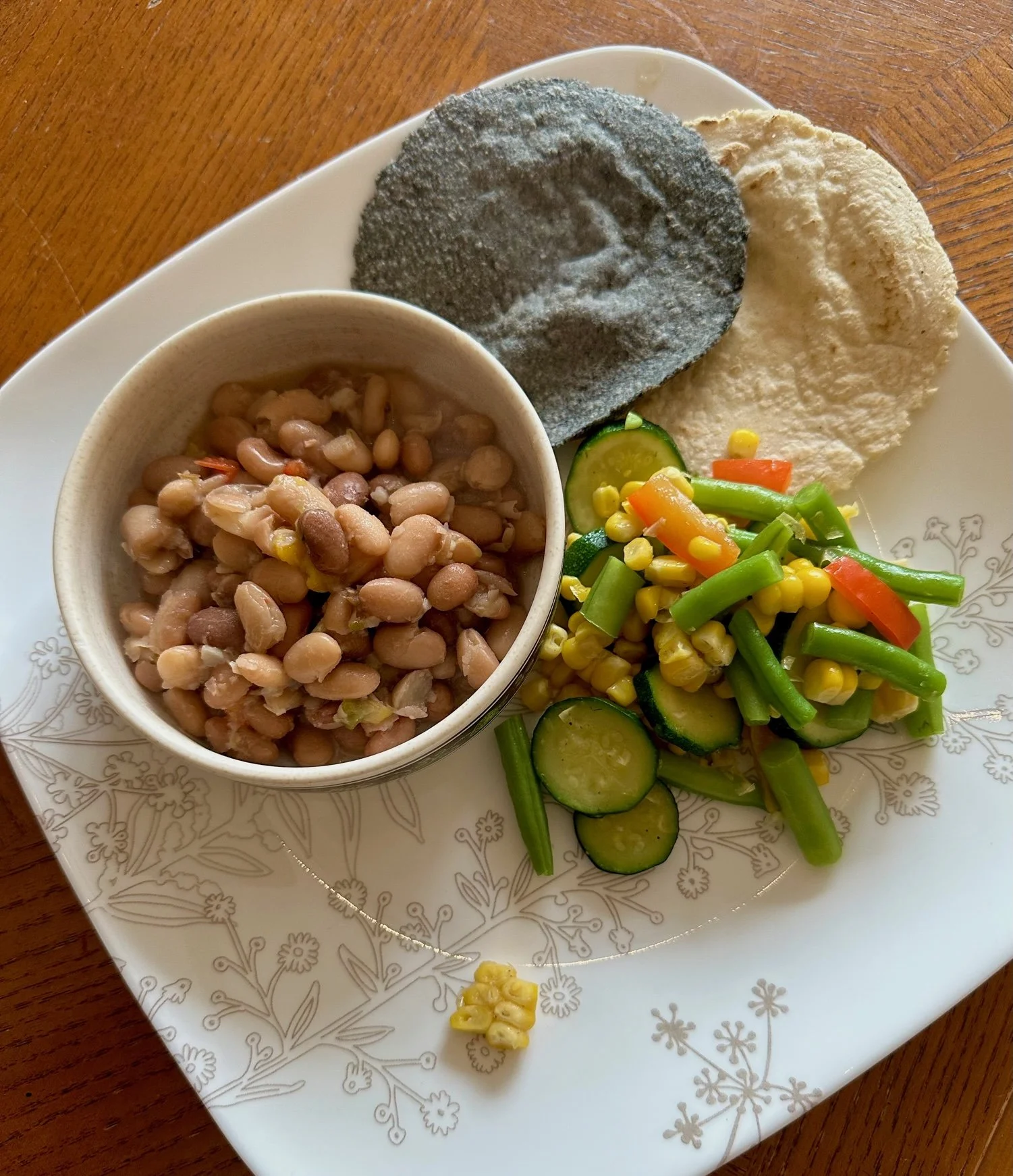 Plate with a serving of cooked pinto beans, a cucumber and mixed vegetable salad, and two types of traditional African flatbreads, one black and one white.