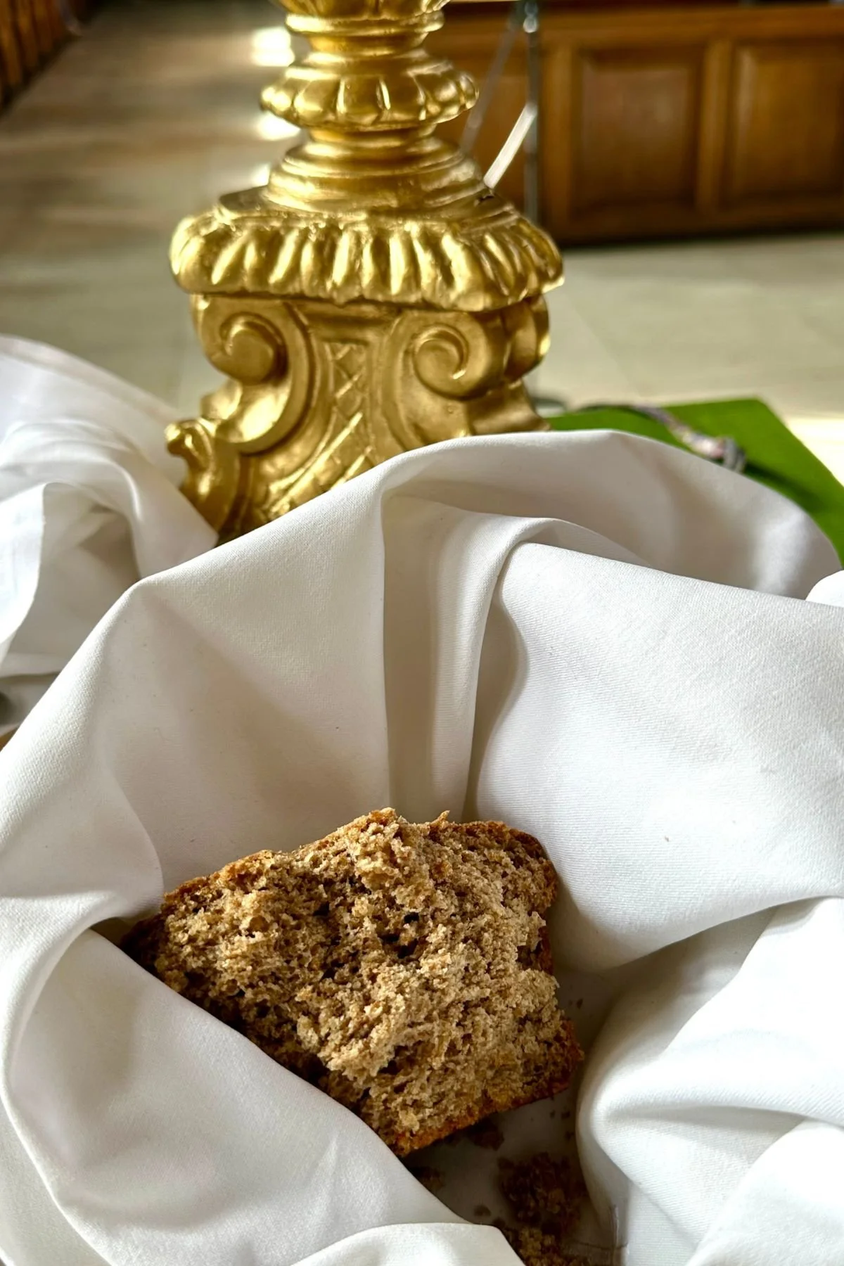 A crumbly piece of baked good placed on white fabric near a gold-colored decorative lamp base.