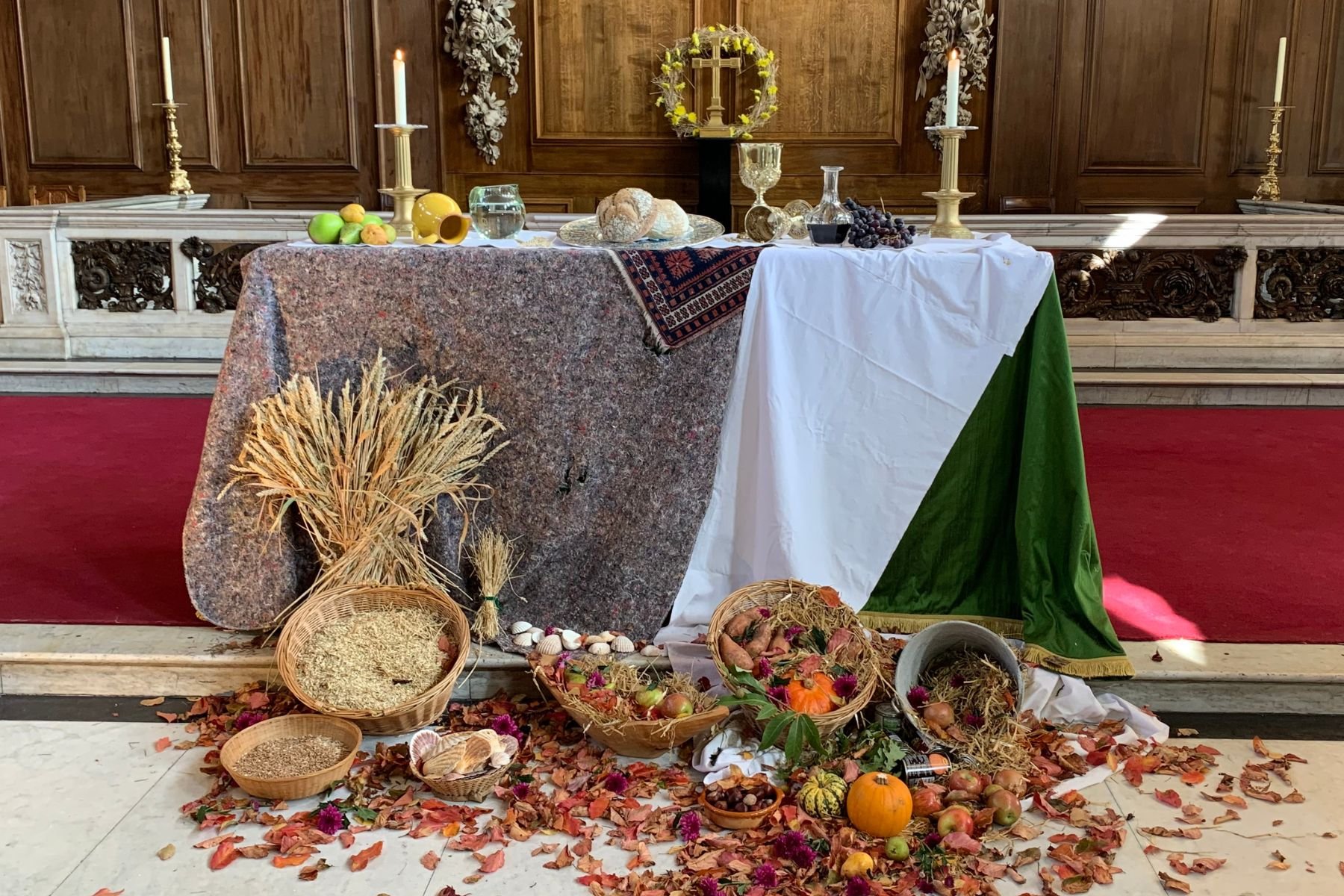 An altar of St James's Church Piccadilly, decorated for the Harvest festival with wheat sheaves, fruits, grains, and pumpkins, surrounded by autumn leaves.