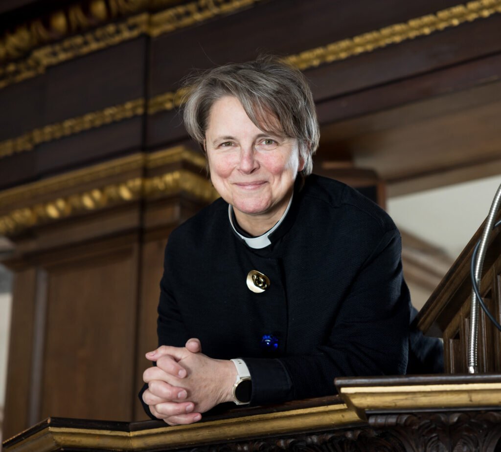 Rev Lucy Winkett smiles at the camera. She is leaning over a balcony inside St James's Church Piccadilly.