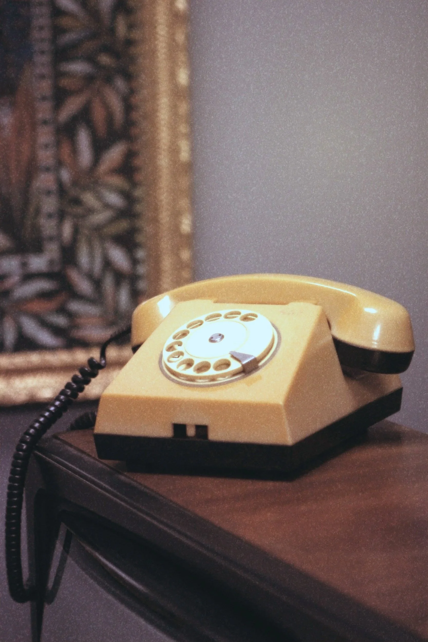 A vintage yellow rotary telephone resting on a wooden surface.