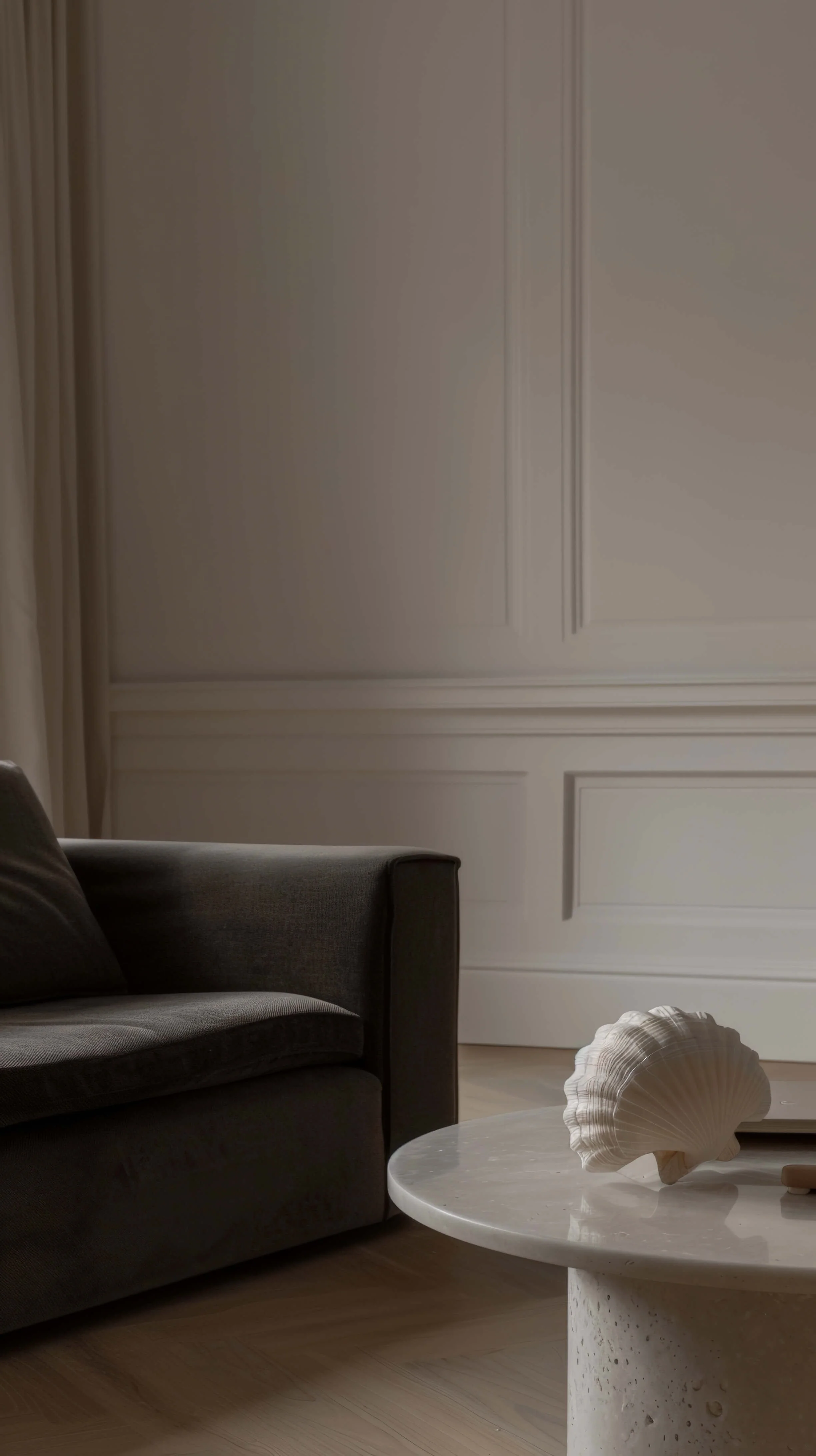 A living room corner with a dark grey sofa, a white marble coffee table with a large seashell decoration, and white wall molding.