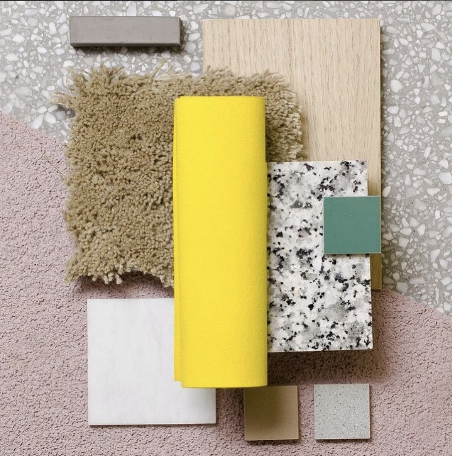 A top view of various interior design material samples, including fabric, wood, paint, and stone textures, arranged on a terrazzo surface.