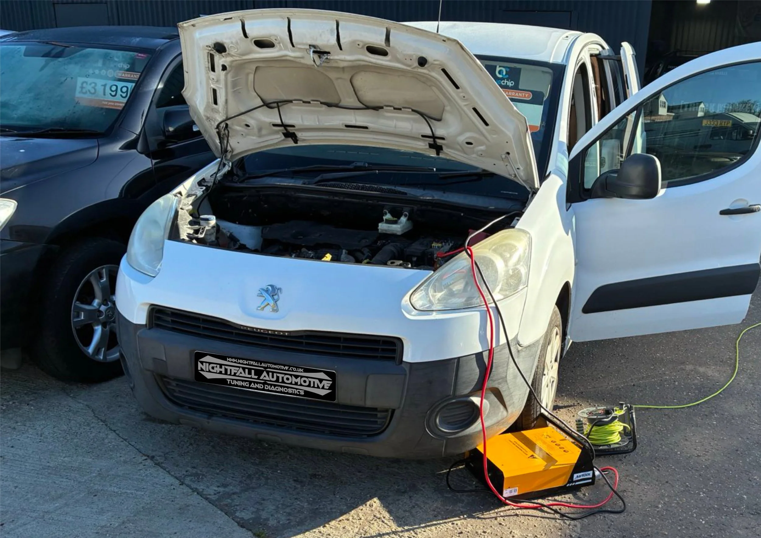 White Peugeot car with hood open and diagnostic equipment connected, parked beside a black car in a lot.