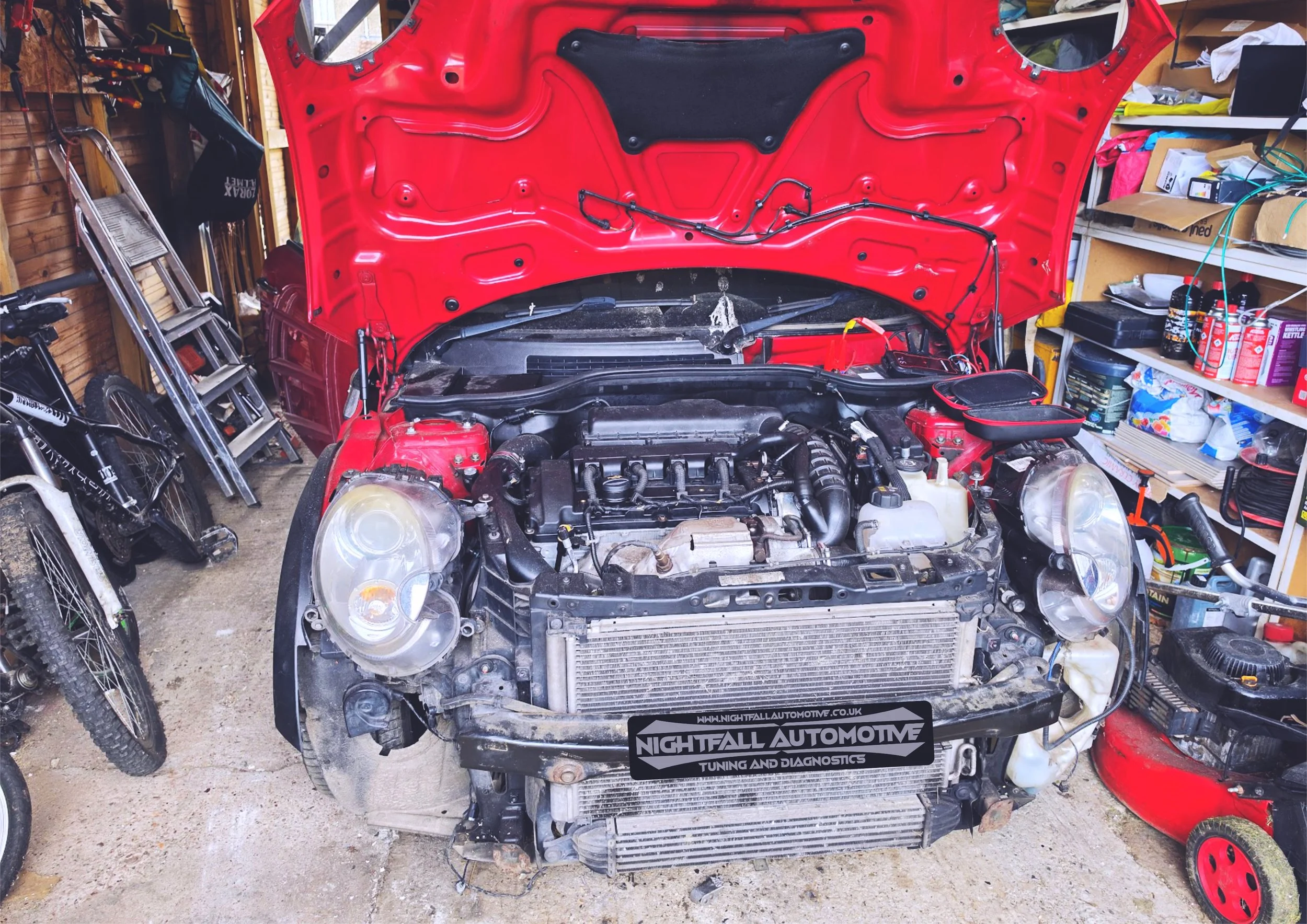 The image shows a red car with its hood open, parked in a garage or workshop. Tuned by nightfallautomotive