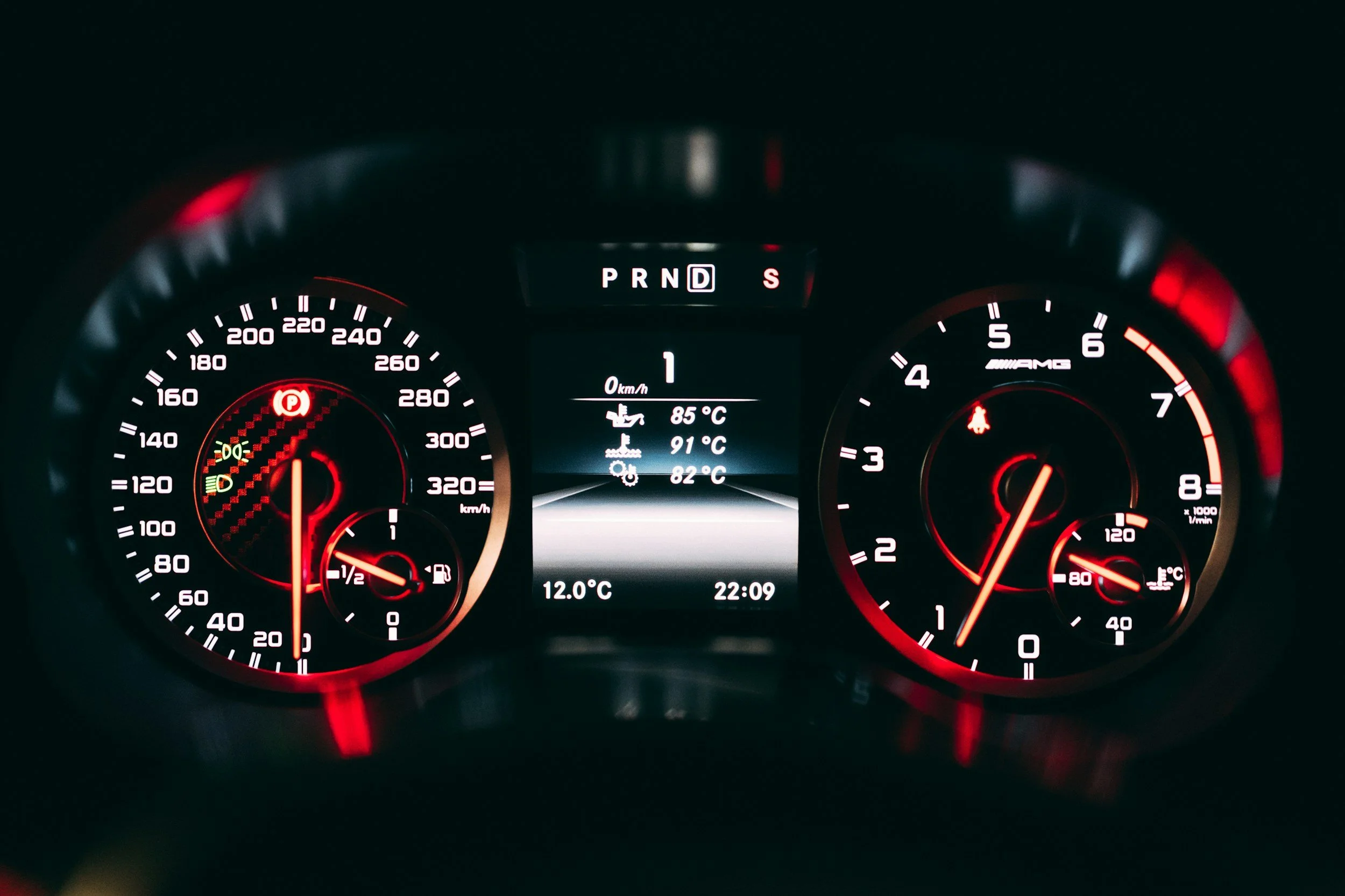 Close-up of a car dashboard at night showing speedometer, tachometer, and digital display with temperature and time, illuminated in red and white.