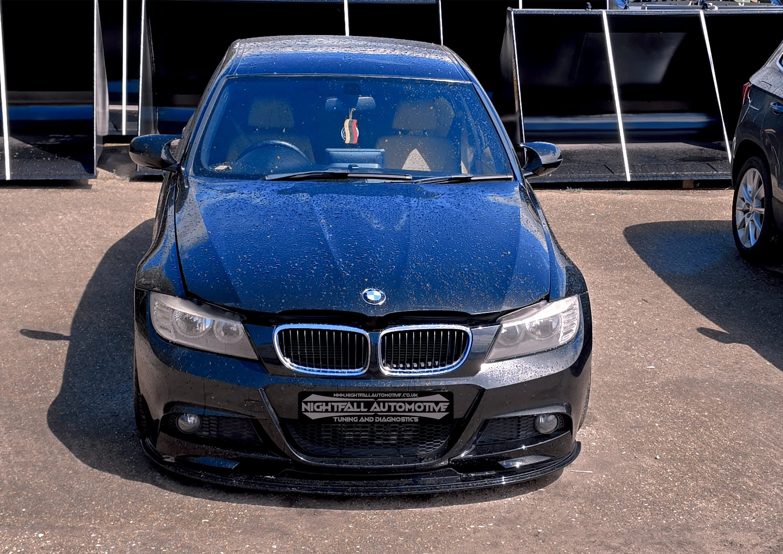 Black BMW car parked at a dealership with a sign for Nightfall Automotive in front.