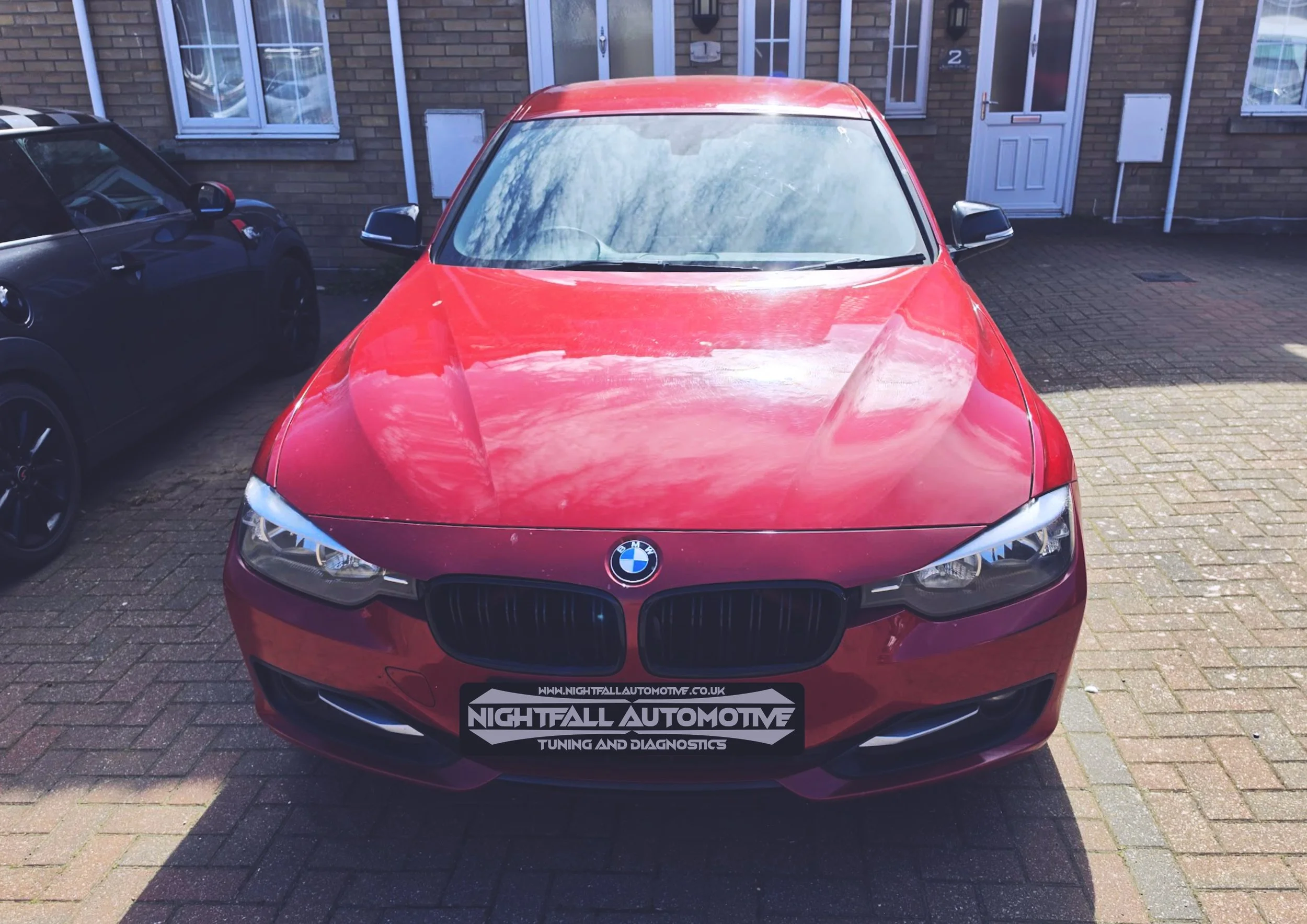 Red BMW parked on a driveway in front of a residential building with a sign for Nightfall Automotive on the front license plate. Stage 1 sorted by Nightfall Automotive