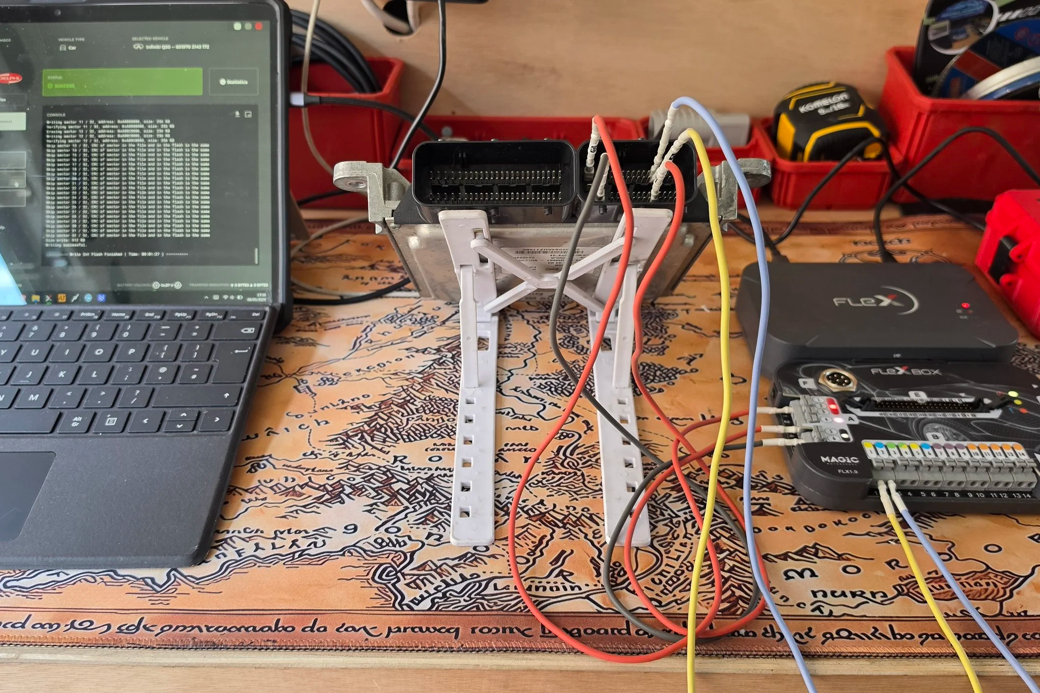 A computer setup on a wooden desk with a laptop, a network device with multiple colored cables connected, Nightfall Automotive tuning and diagnostics
