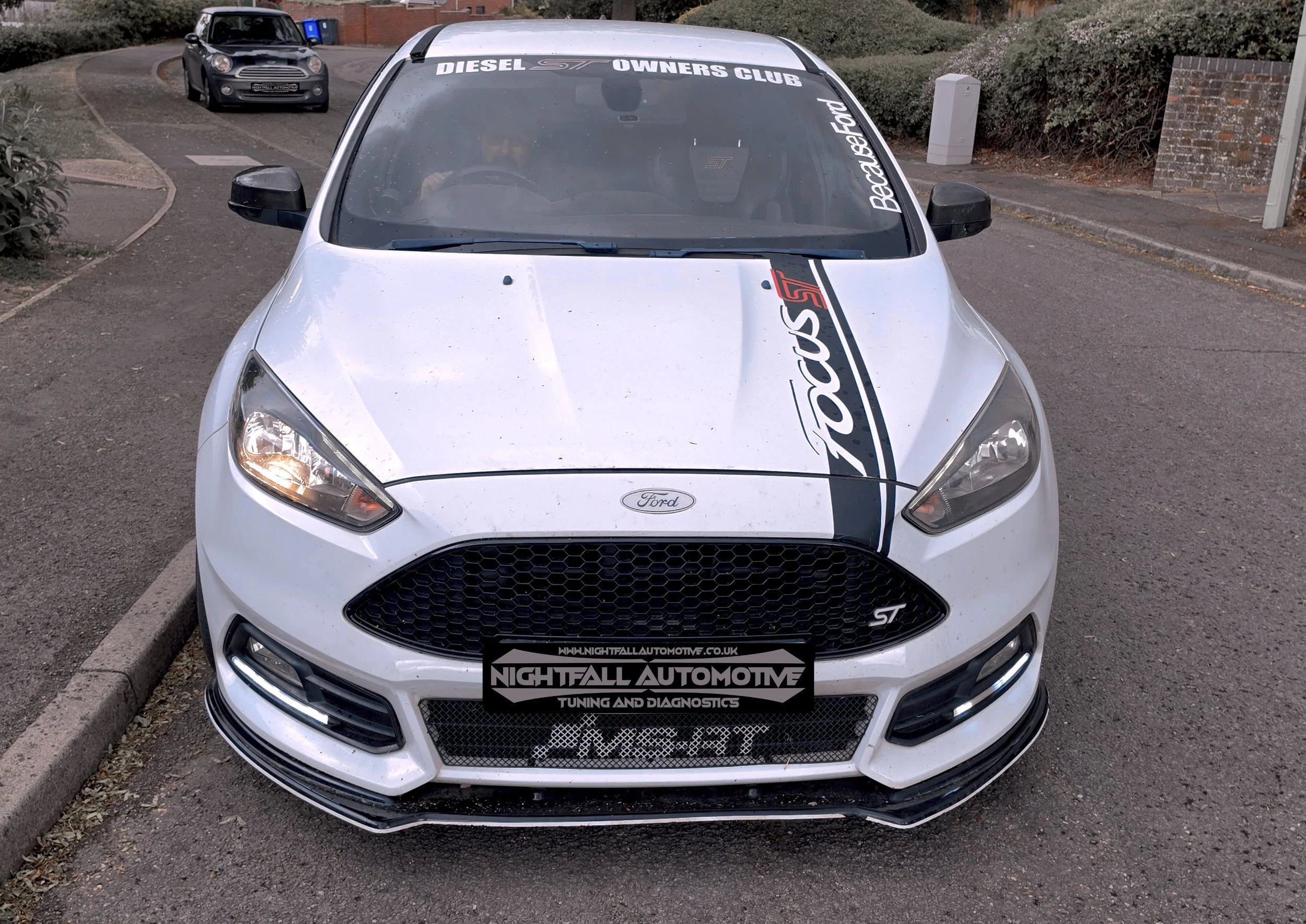 White Ford Fiesta ST with decals on the hood and windshield, parked on a street, Tuned by Nightfall Automotive