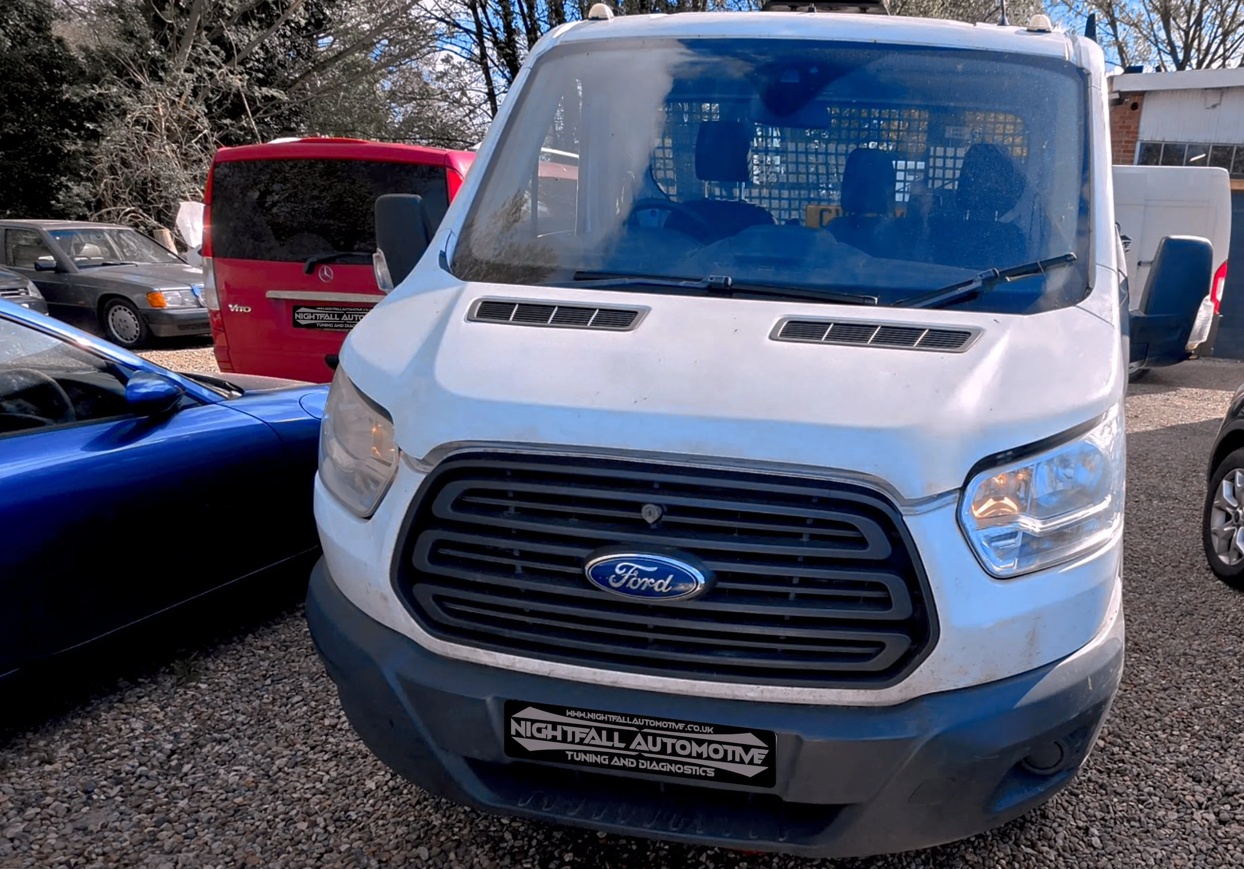 A white Ford van parked outdoors with other vehicles around, a sign reading 'NIGHTFALL AUTOMOTIVE TUNING AND DIAGNOSTICS' on the front bumper.