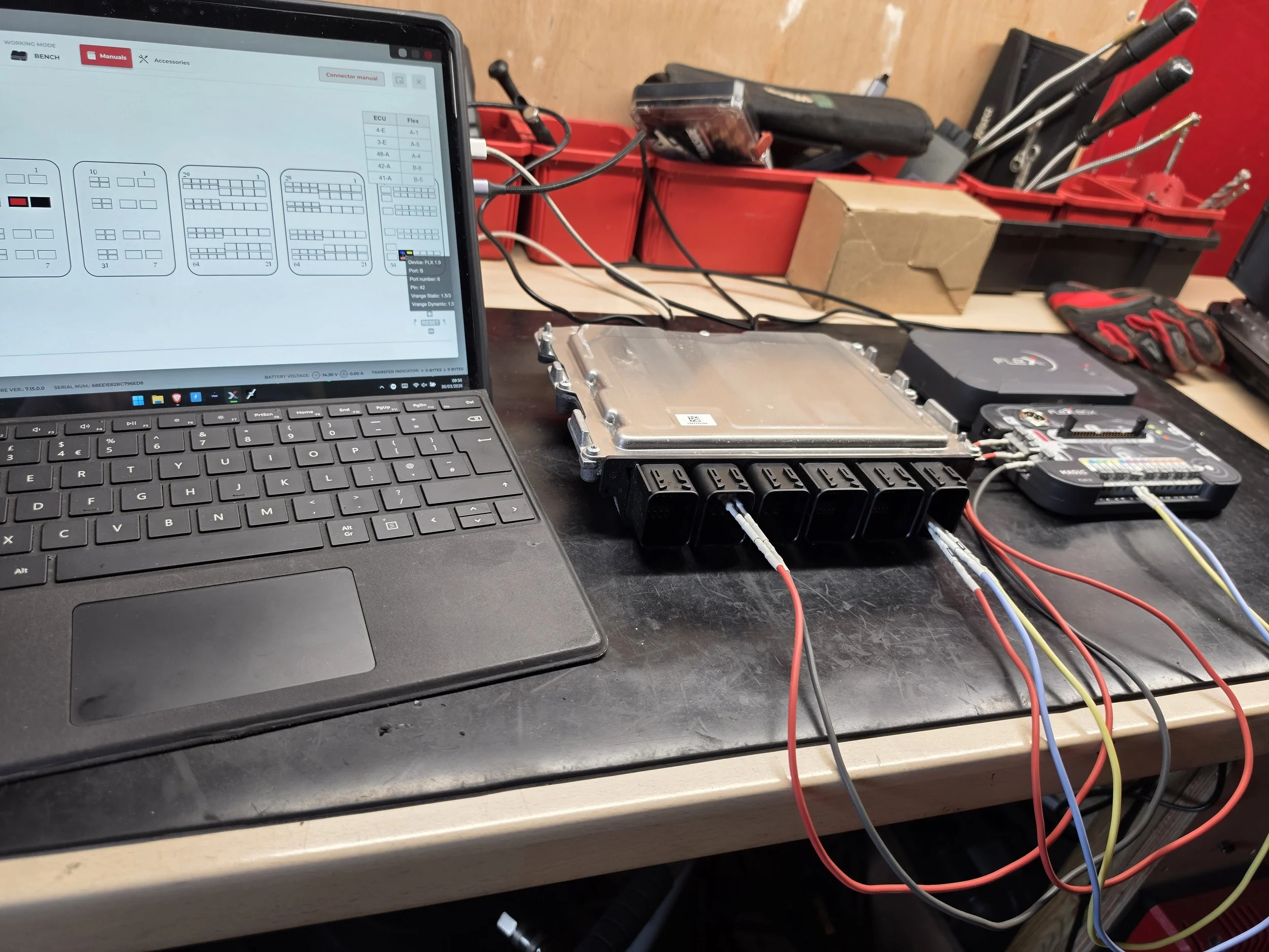A workbench with a laptop displaying a circuit diagram, connected to electronic components including an ECU and wiring harness, Nightfall Automotive EGR Solution
