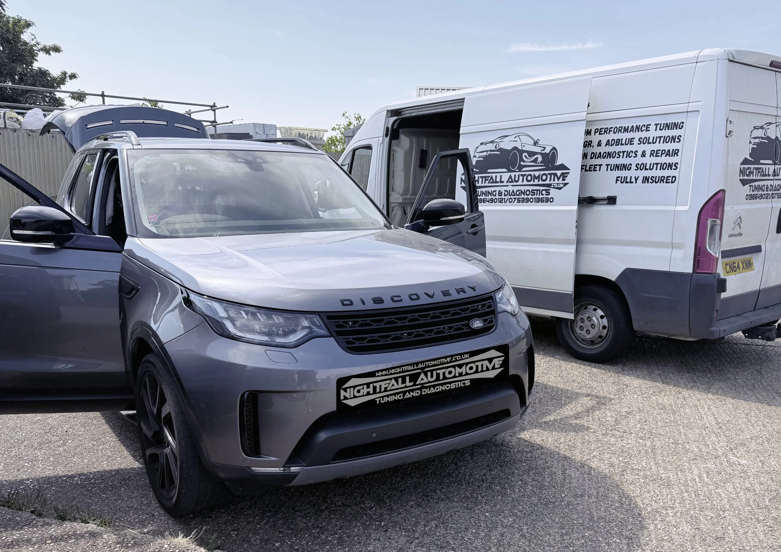 A silver Land Rover Discovery parked in front of a white van with branding for Nightfall Automotive, a tuning and diagnostics shop, on a sunny day.
Tuned by Nightfall Automotive
