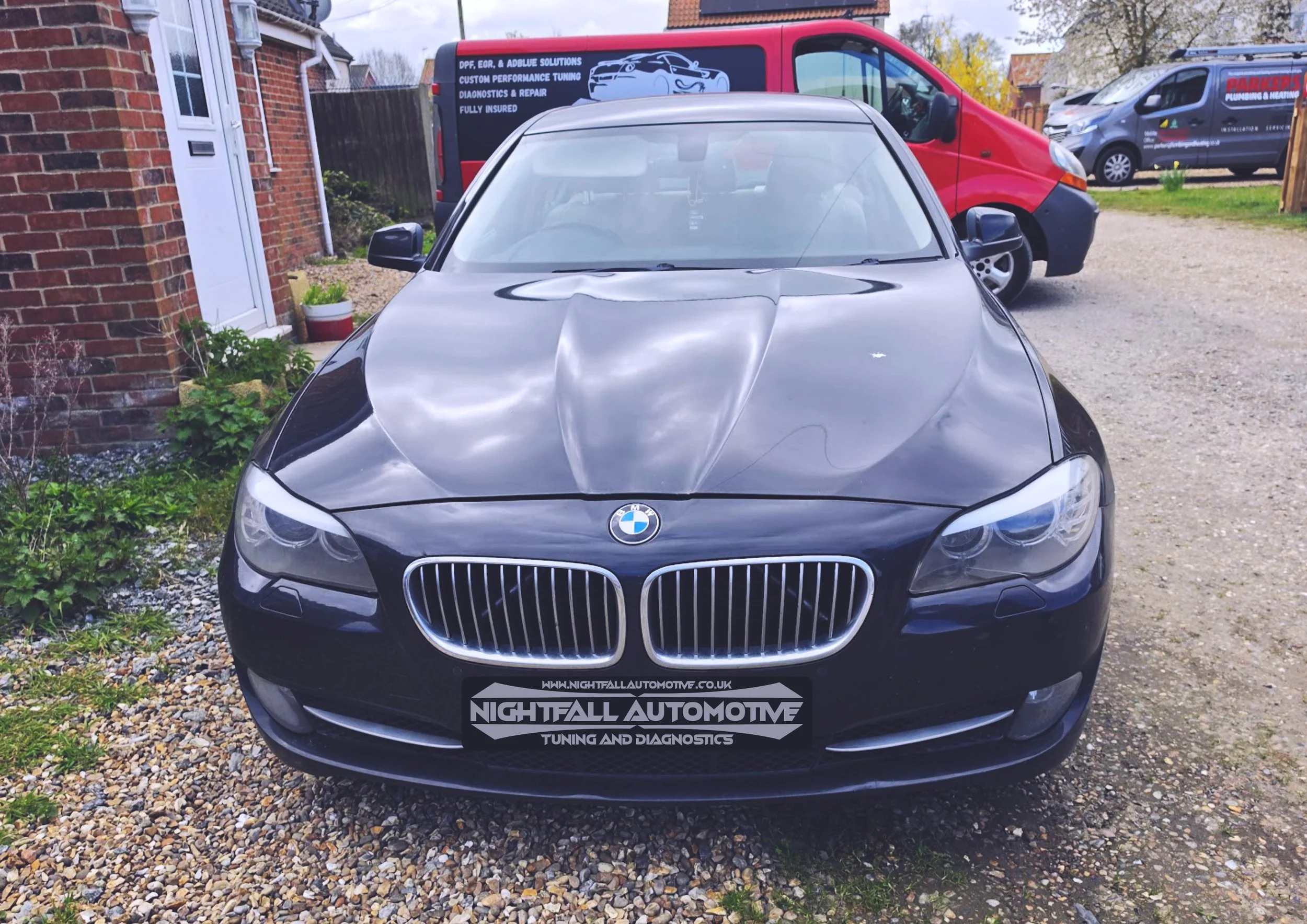 Black BMW car parked outdoors with a view of the front, showing the grille, headlights, and a sign on the front bumper reading 'Nightfall Automotive Tuning and Diagnostics.'