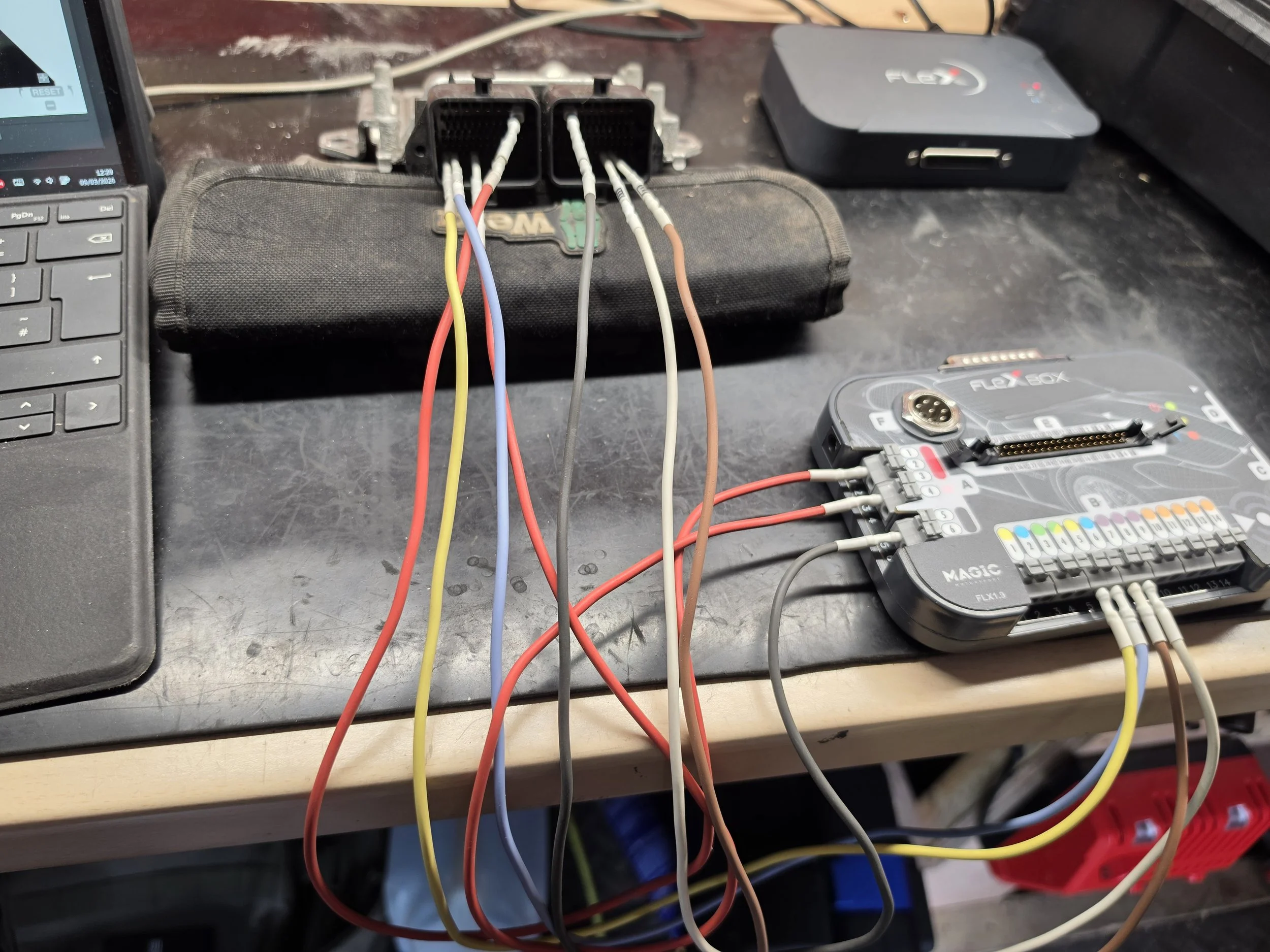 Automotive wiring harness connected to a vehicle's electronic control module (ECU), with wires organized and connected to diagnostic equipment on a workbench.