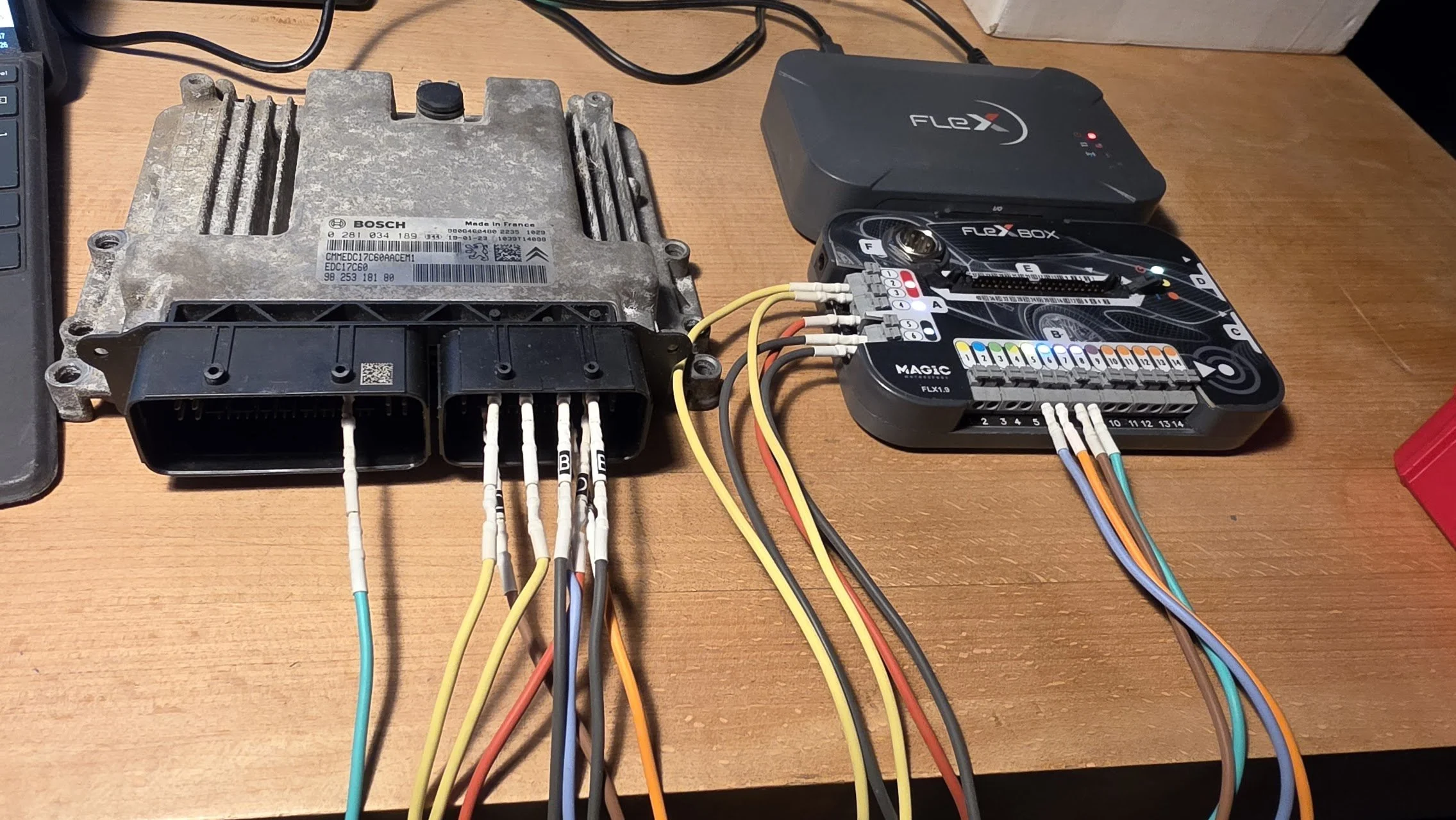Car electronic control module connected to a wiring harness and a diagnostic tool on a wooden table.
