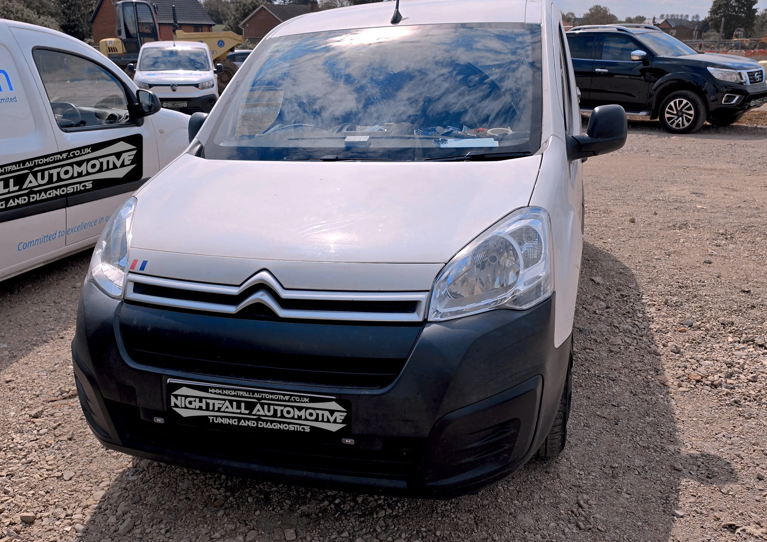 Front view of a silver Citroën van parked on a gravel lot, with multiple vehicles and construction equipment in the background. Tuned by Nightfall Automotive