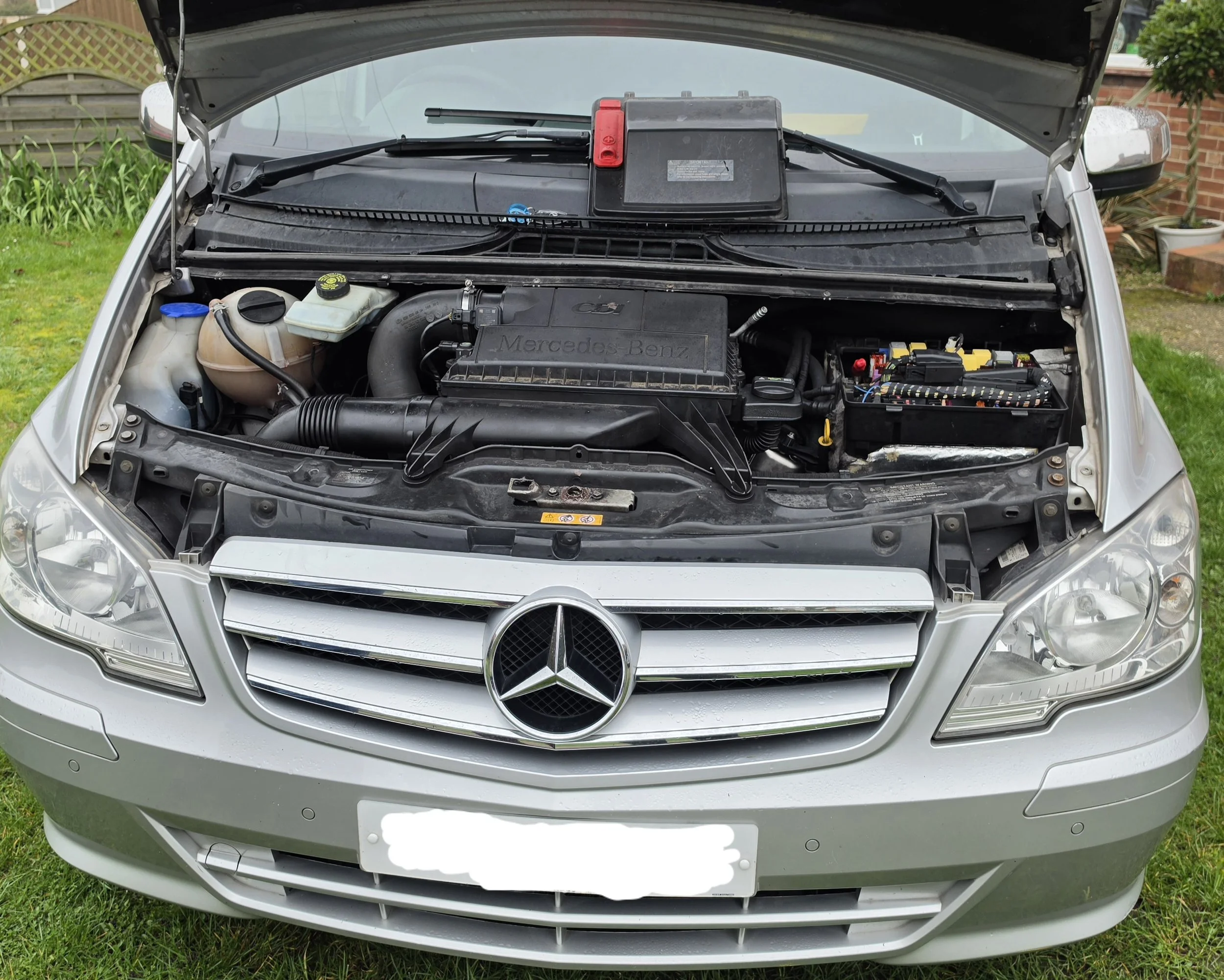 Front view of a silver Mercedes-Benz car with the hood open, showing the engine compartment and various engine components.