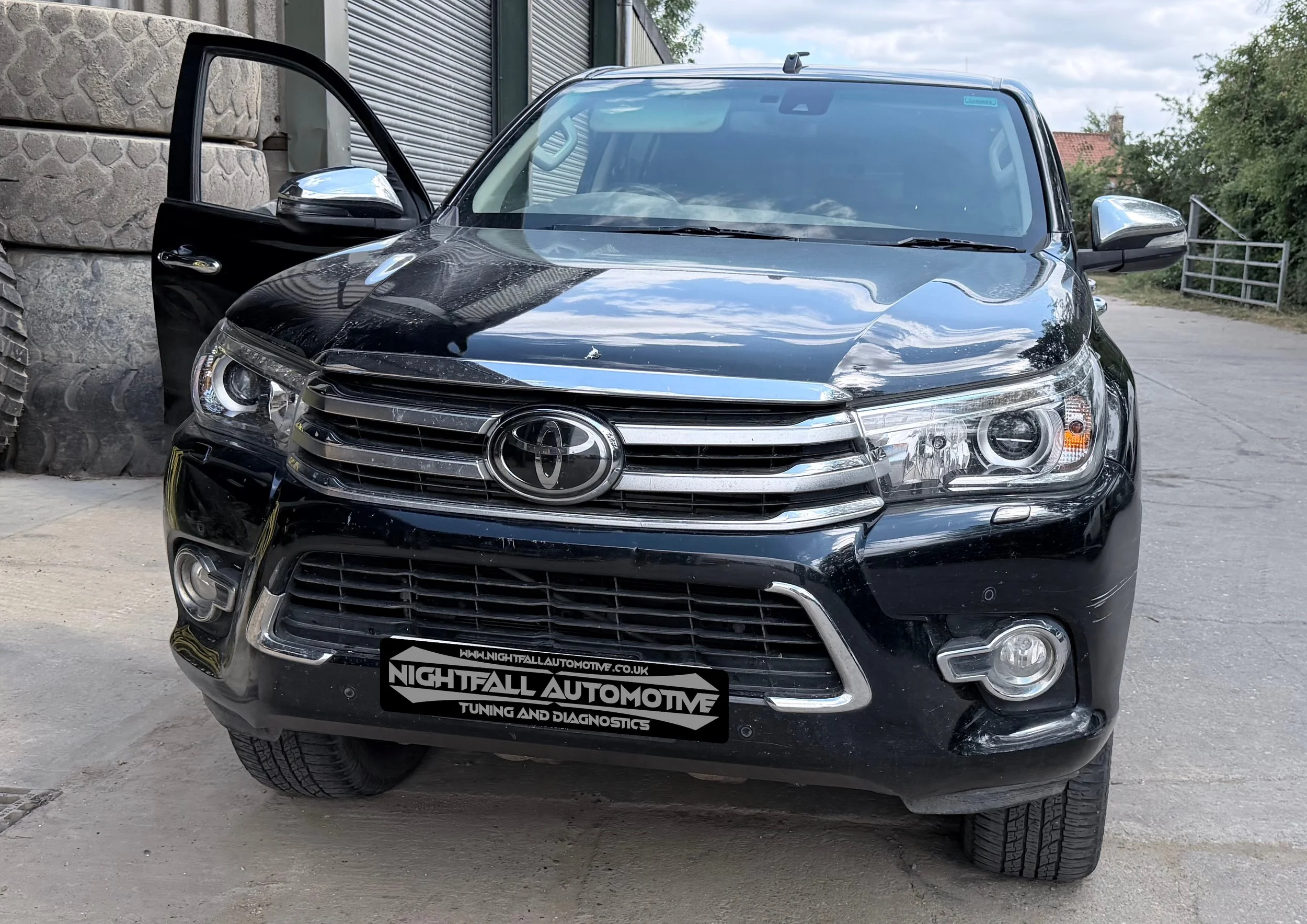A black Toyota SUV parked outdoors with the front driver's side door open, displaying a logo that reads 'Nightfall Automotive' on the front license plate area, Tuned by Nightfall Automotive