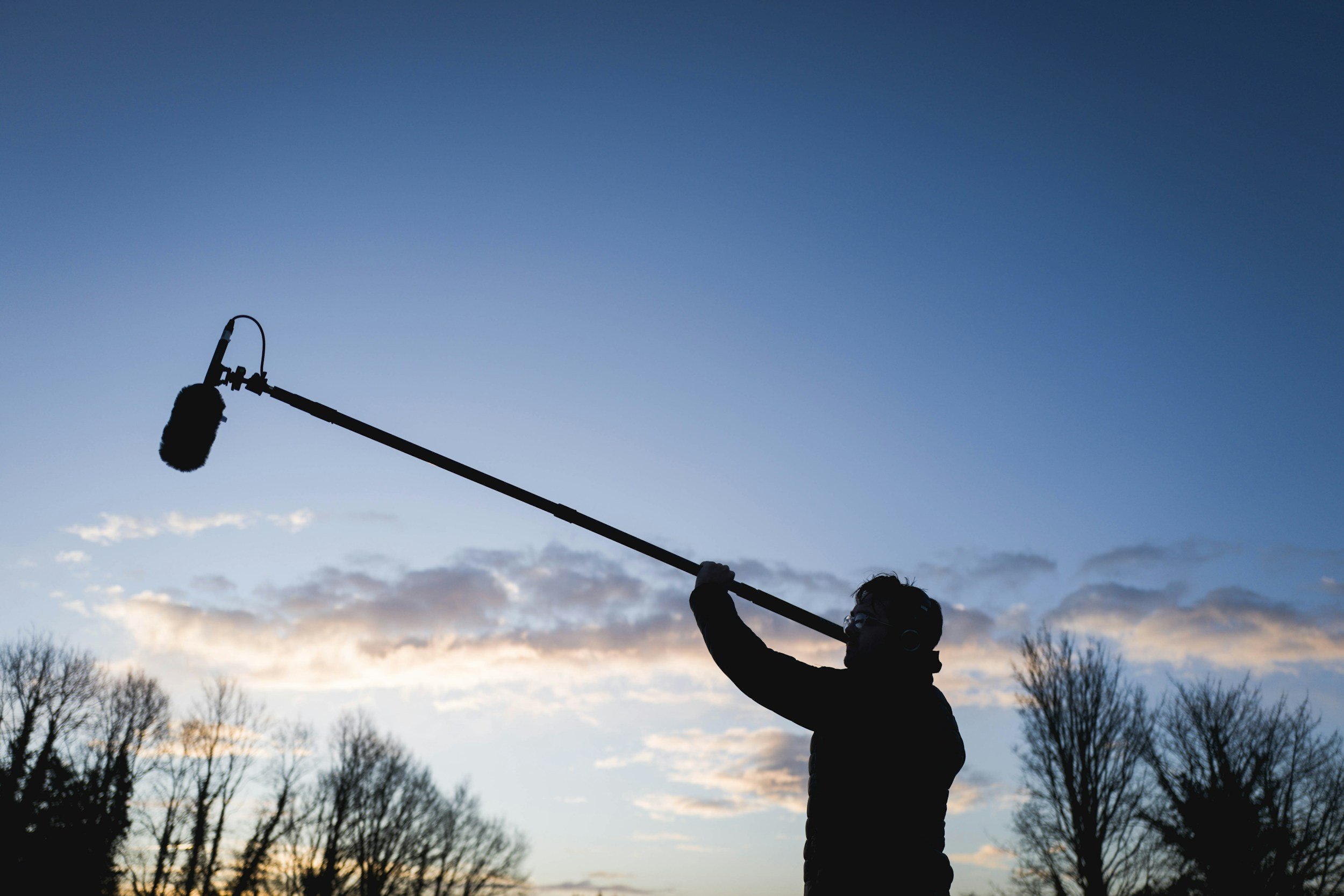 Boom operator recording location sound at sunset