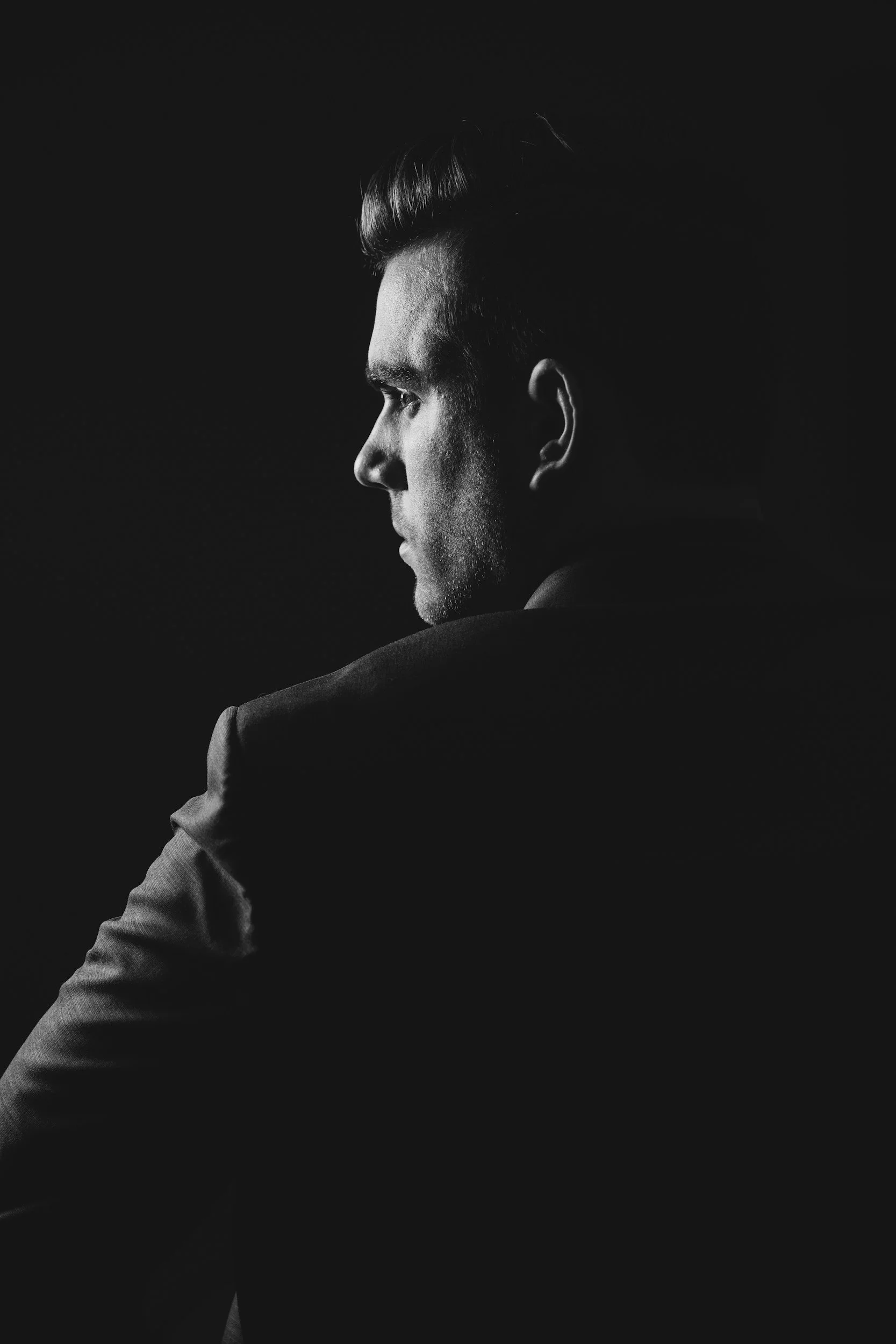 Black and white portrait of a man in profile, looking to the left, with short, styled hair and wearing a suit