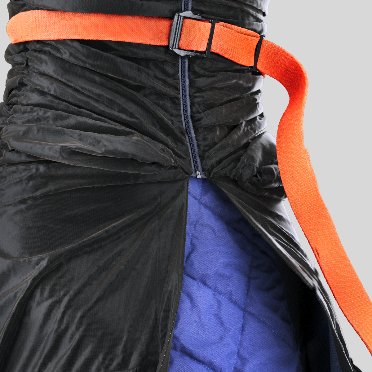 Close-up of a person wearing a black puffer jacket, blue quilted inner layer, and an orange belt.