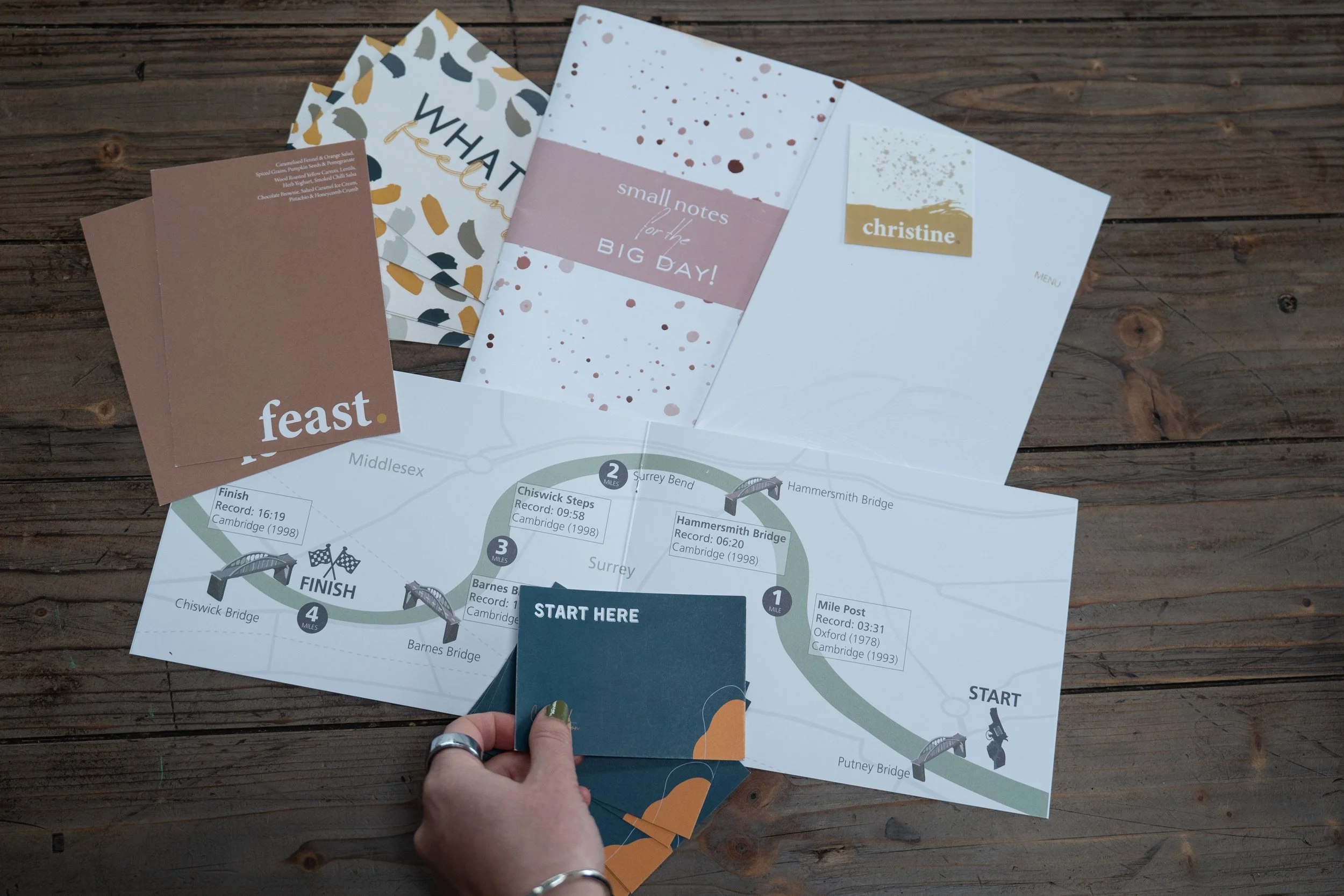 A virtual assistant holding a design of a place card with other designs like notebooks and brochures spread around her on a wooden table