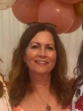 Woman with wavy hair smiling, surrounded by pink and yellow balloons.