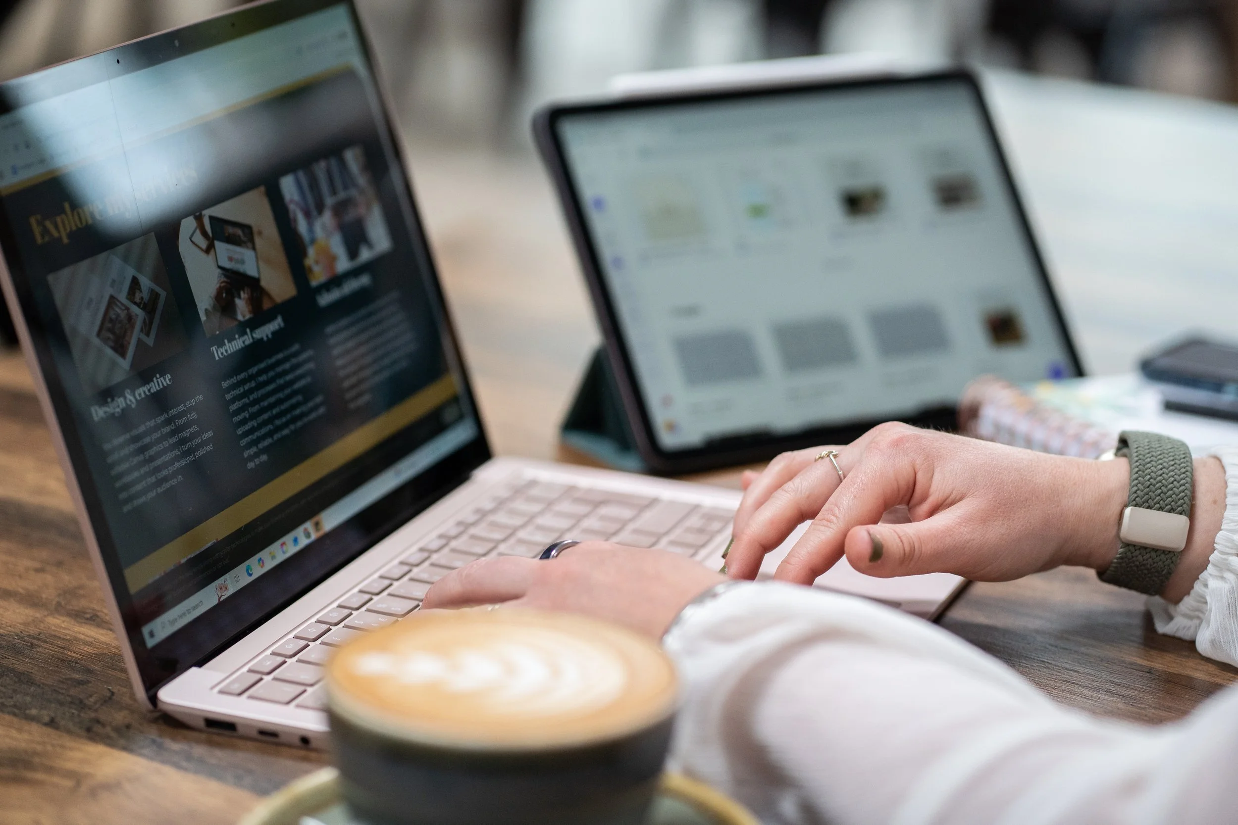 A virtual assistant working on a laptop with a tablet nearby, and a cup of coffee in the foreground.