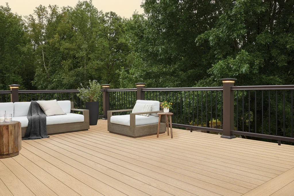 Outdoor wooden deck with white patio furniture and lush green trees in the background.