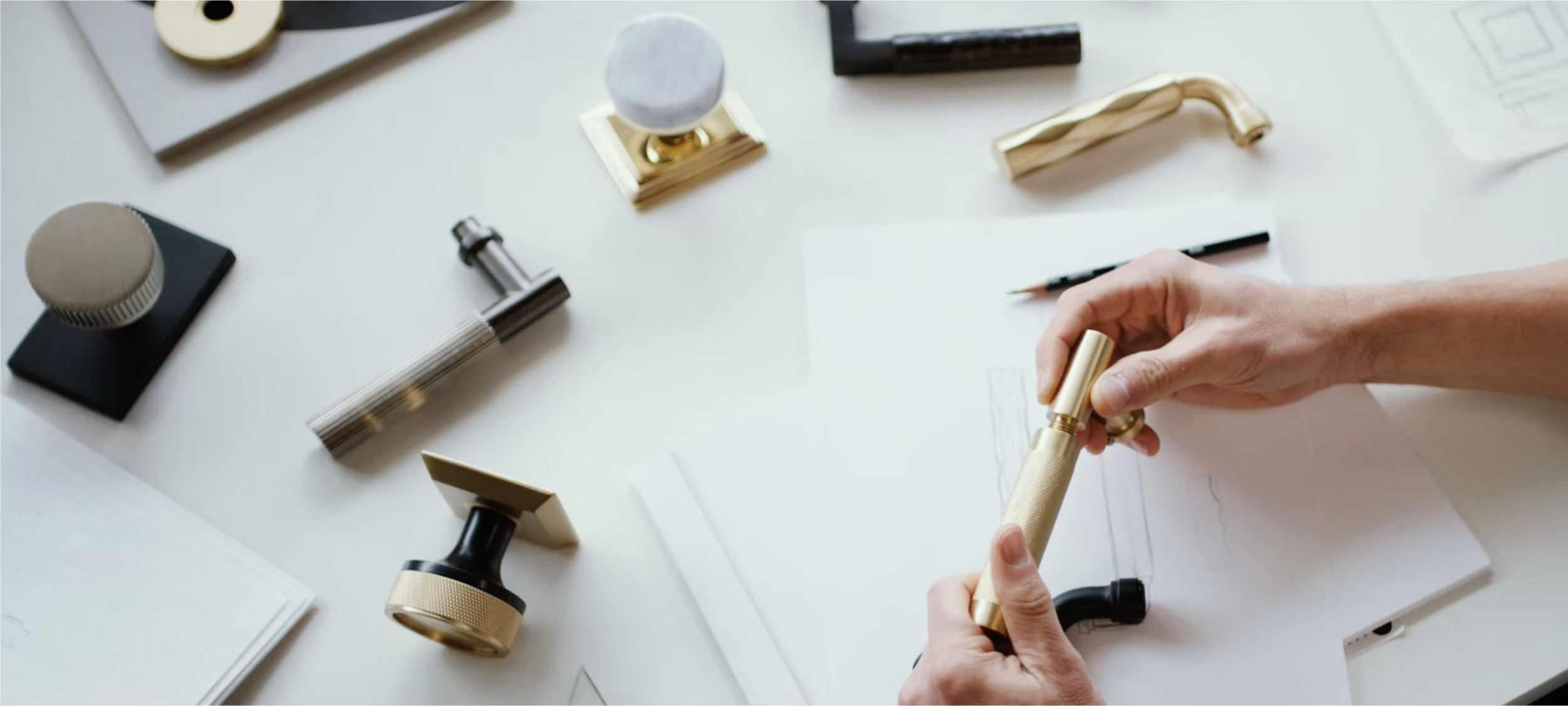 Hands stamping paper with a gold-branded rubber stamp on a white desk surrounded by various stamping tools, ink pads, paper, and a pencil.