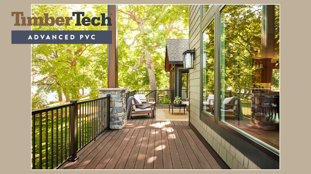 A screened porch with wood flooring, outdoor furniture, large windows, and lush green trees in the background.