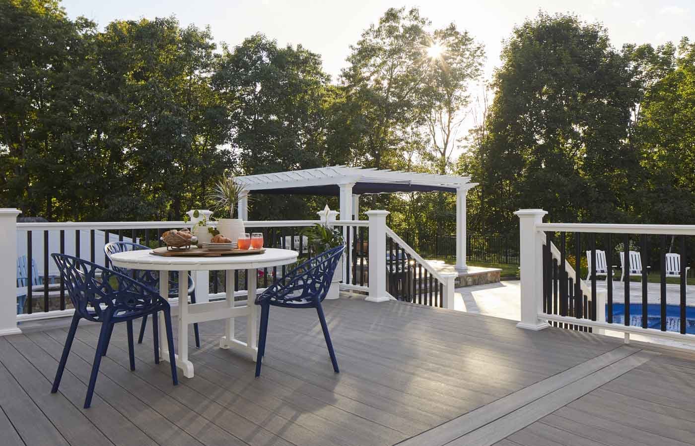 Decorated outdoor deck with a round table and four navy blue chairs, surrounded by white railing, with trees in the background and a clear sky