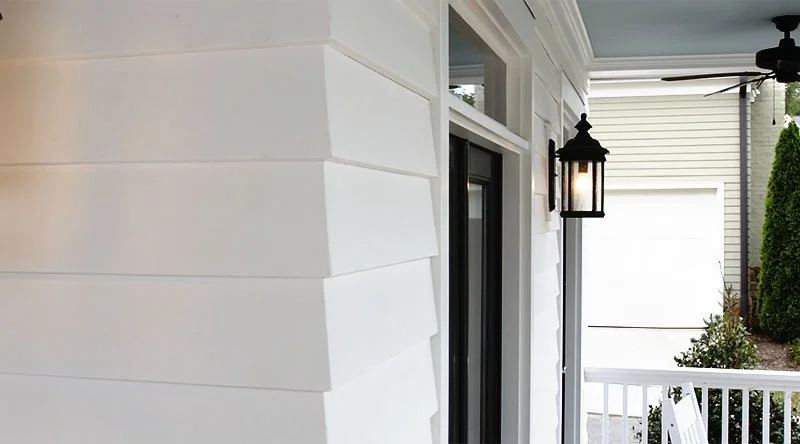 Close-up of a house's exterior wall with white siding and a porch with a black lantern-style light fixture.