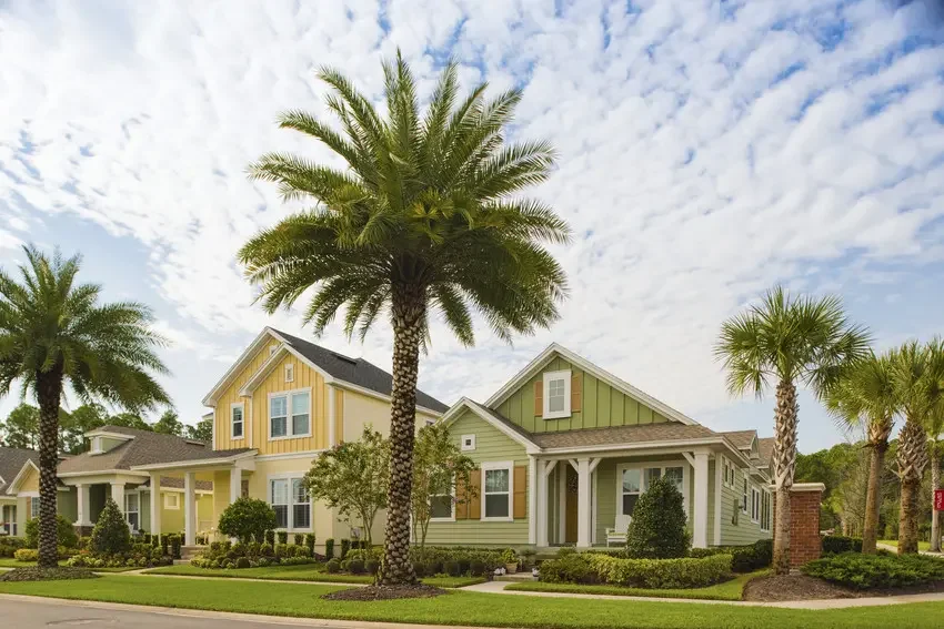 Colorful houses with lush landscaping and palm trees in front, under a partly cloudy sky.