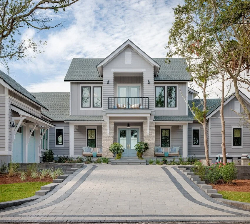 Front view of a modern two-story house with a gray exterior, front porch with two benches, a small balcony, and well-maintained landscaping.