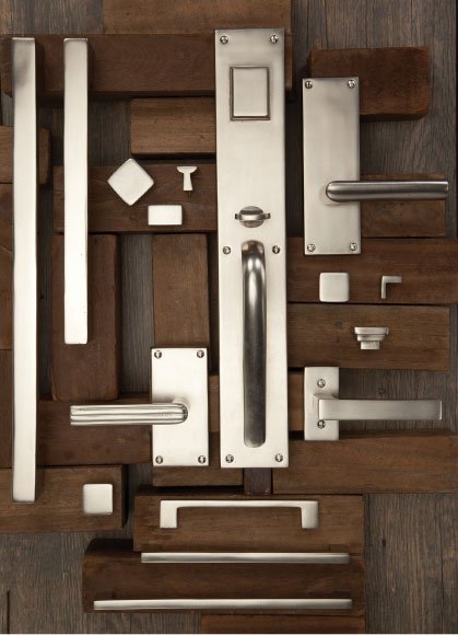 Assorted door handles, knobs, and metal plates arranged on hardwood floor.